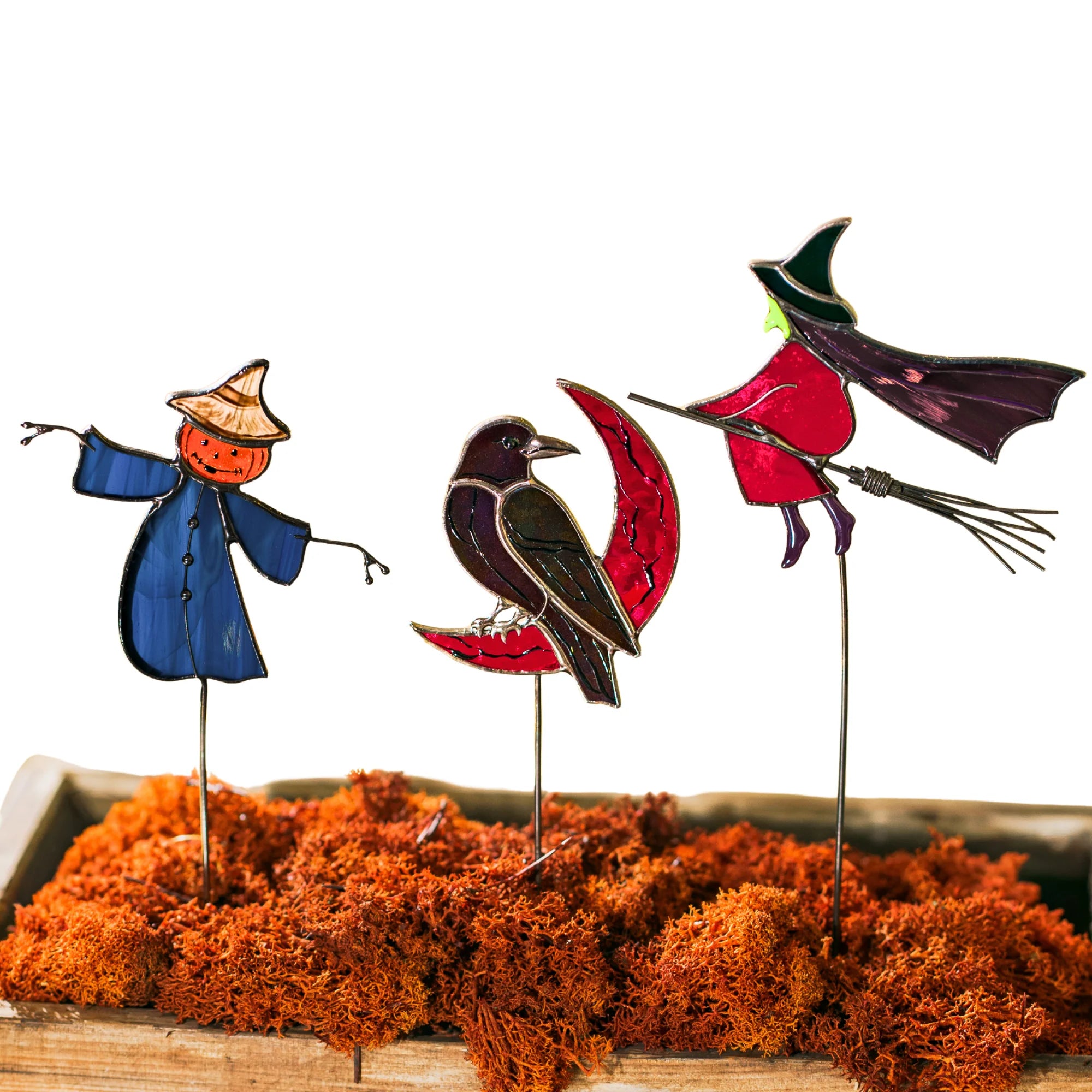 Set of three Halloween stained glass plant stakes on a white background - blue-coated scarecrow with a jack-o-lantern head, raven on a red crescent moon and a flying witch