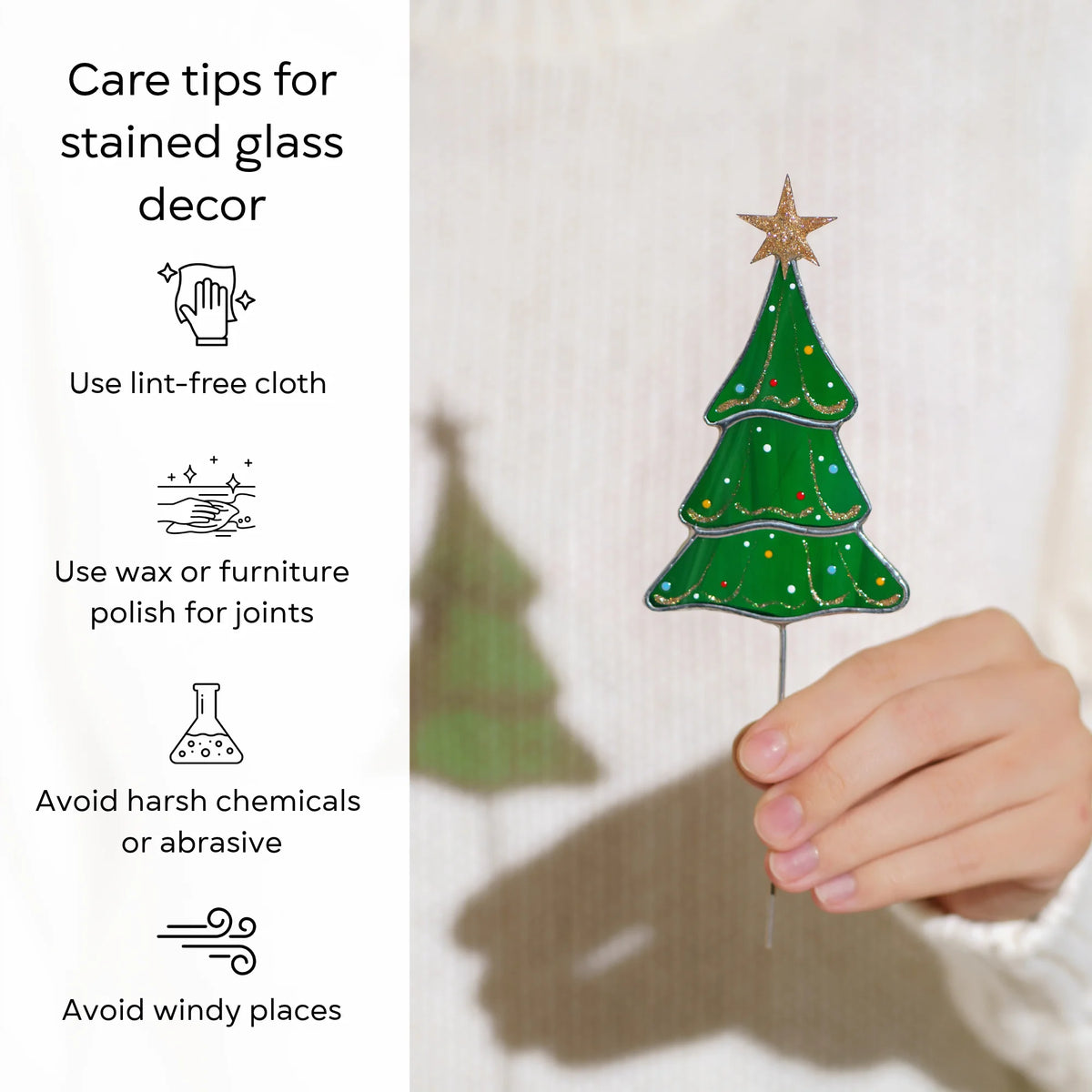 Hand holding the Christmas tree stained glass plant stake - care tips: use a lint-free cloth, use wax or furniture polish for the joints, avoid harsh chemicals and windy places