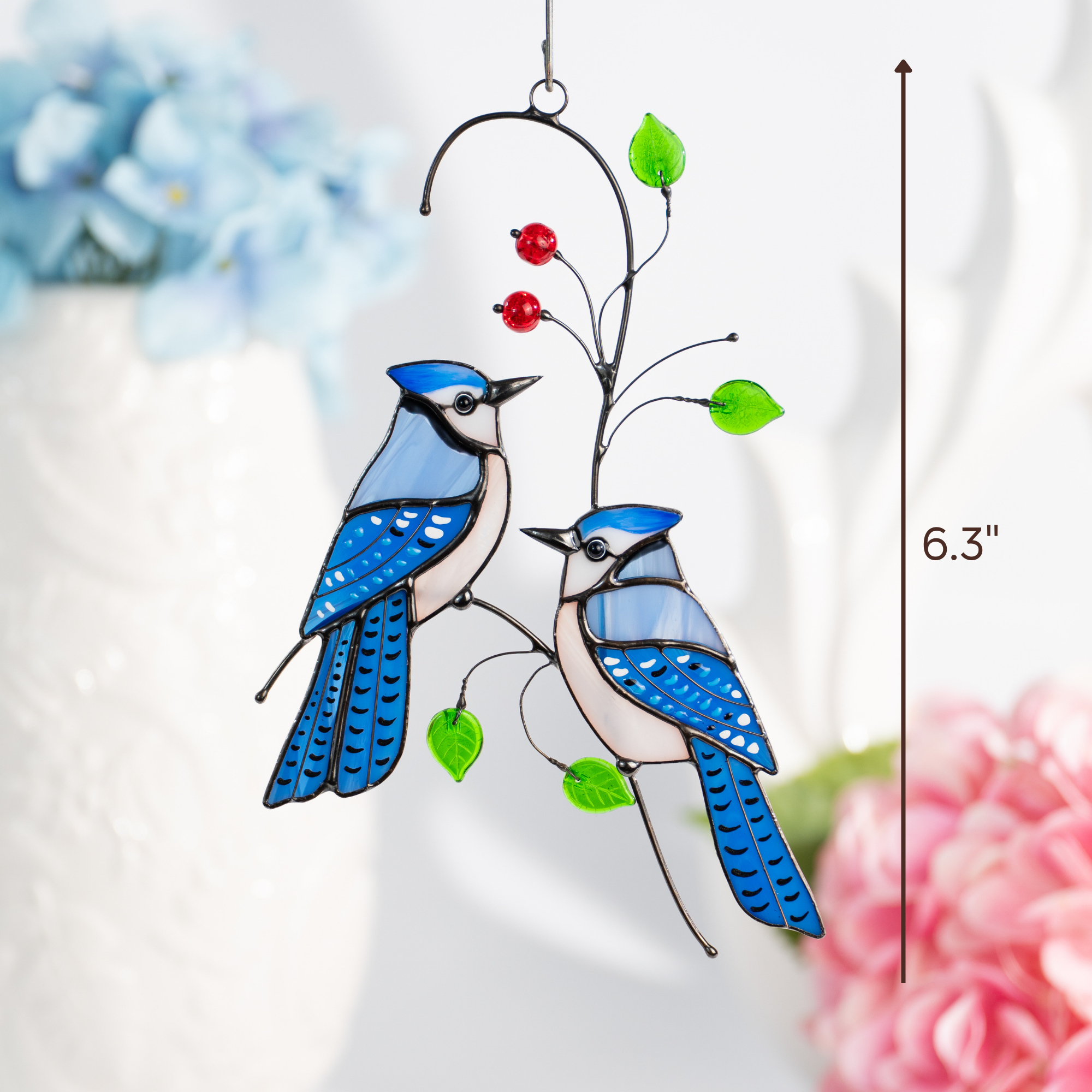 Stained glass blue jay suncatcher hanging near vase with flowers, size indicated as 6.3 inches