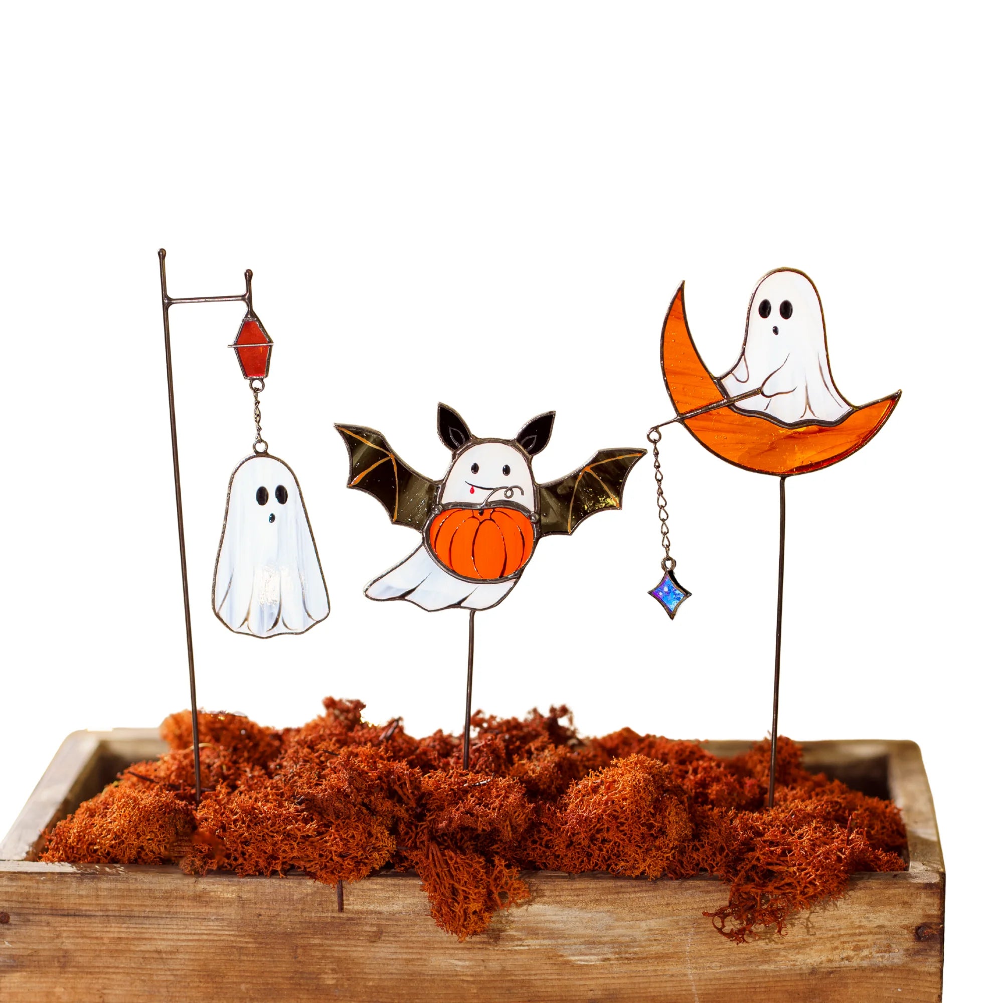 A set of Halloween stained glass ghost decorations nestled in bright orange moss inside a wooden planter against a white background, ideal for holiday gifting.