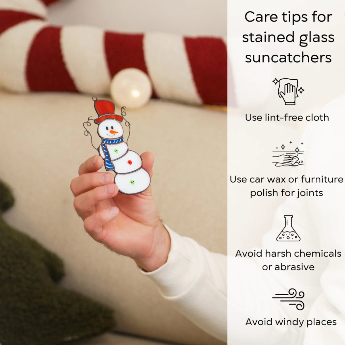 Hand holding the Christmas stained glass snowman suncatcher by a cozy sofa - care for this handmade Christmas decor with a lint-free cloth, wax the solder joints, avoid harsh chemicals and wind