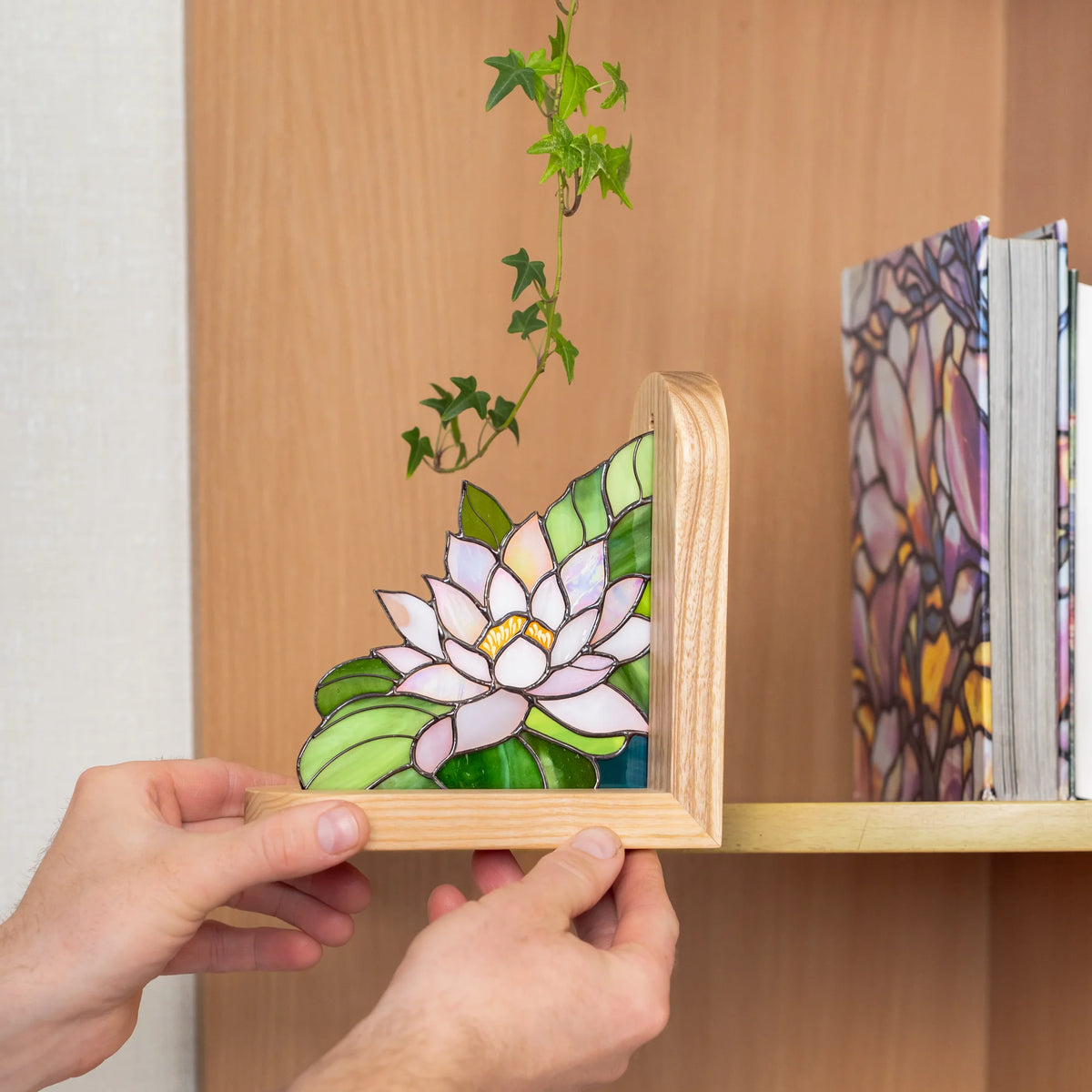 Handmade stained glass water lily bookend holding up books on a wooden shelf, trailing ivy plant nearby - a charming stained glass home library decor accent