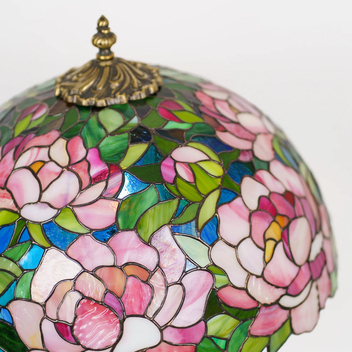 Close-up of the brass pull chain and lit bulb inside a stained glass peony lamp shade, pink glass petals and green leaves glowing softly around it, handmade Tiffany technique table lamp