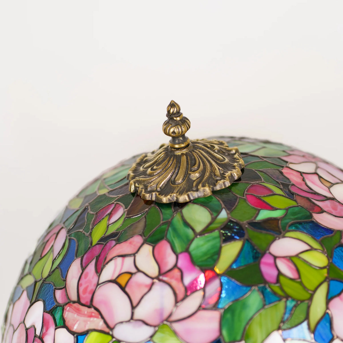 Handmade stained glass peony table lamp glowing on a wooden sideboard beside a bookshelf and sunlit window - a Tiffany style lamp bringing warm floral light to a home office or study