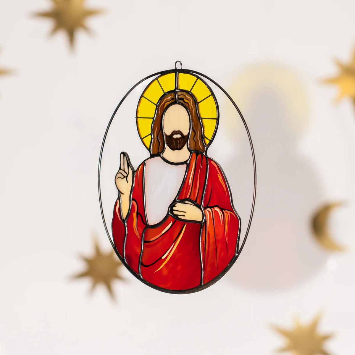 Jesus stained glass suncatcher floating among golden stars and crescent moons, casting a soft colored shadow on the wall - a handmade glass window hanging that brings light and blessing home