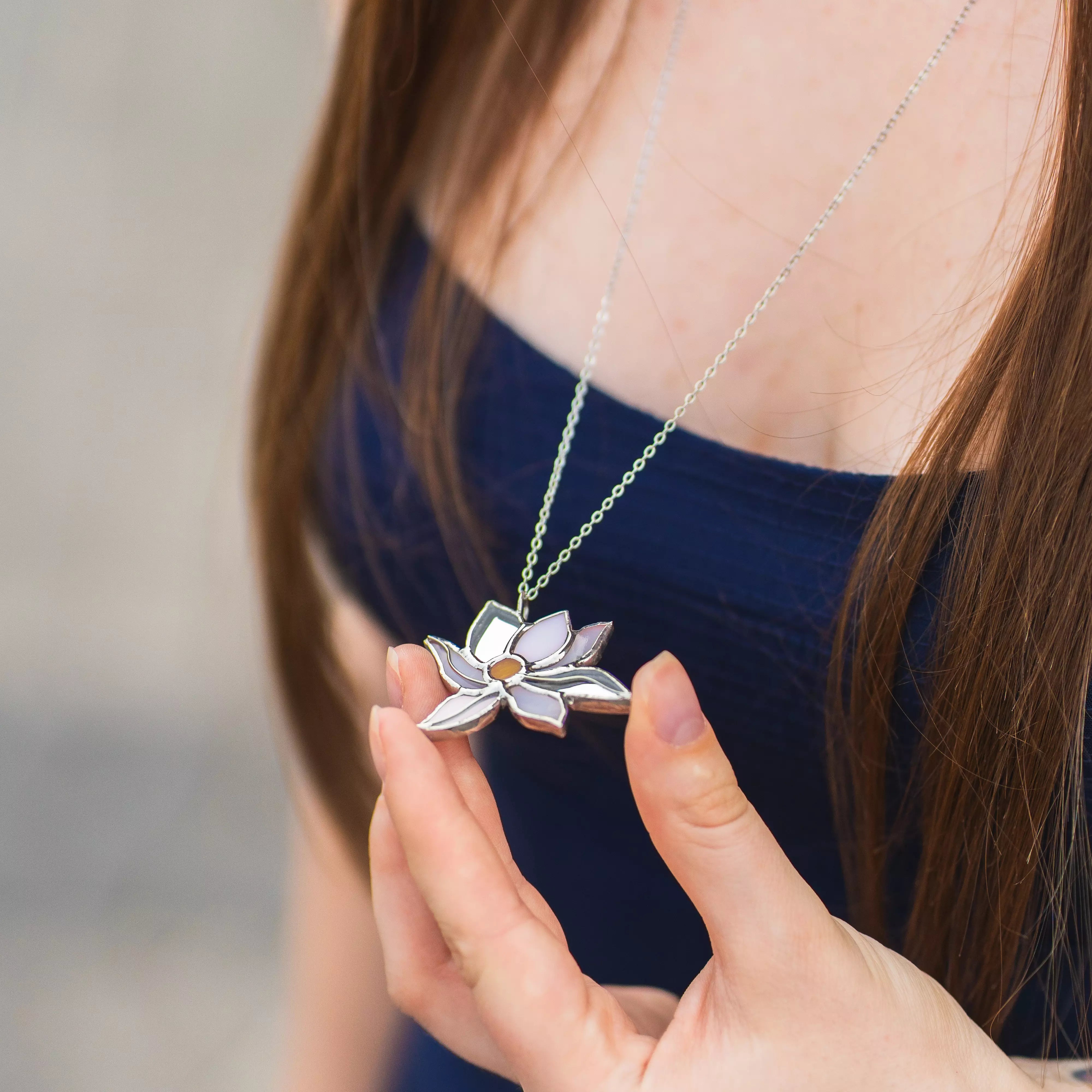 Woman holding the White Lotus stained glass pendant against a navy top, showing the white glass petals and amber center - handmade lotus necklace symbolizing purity and calm