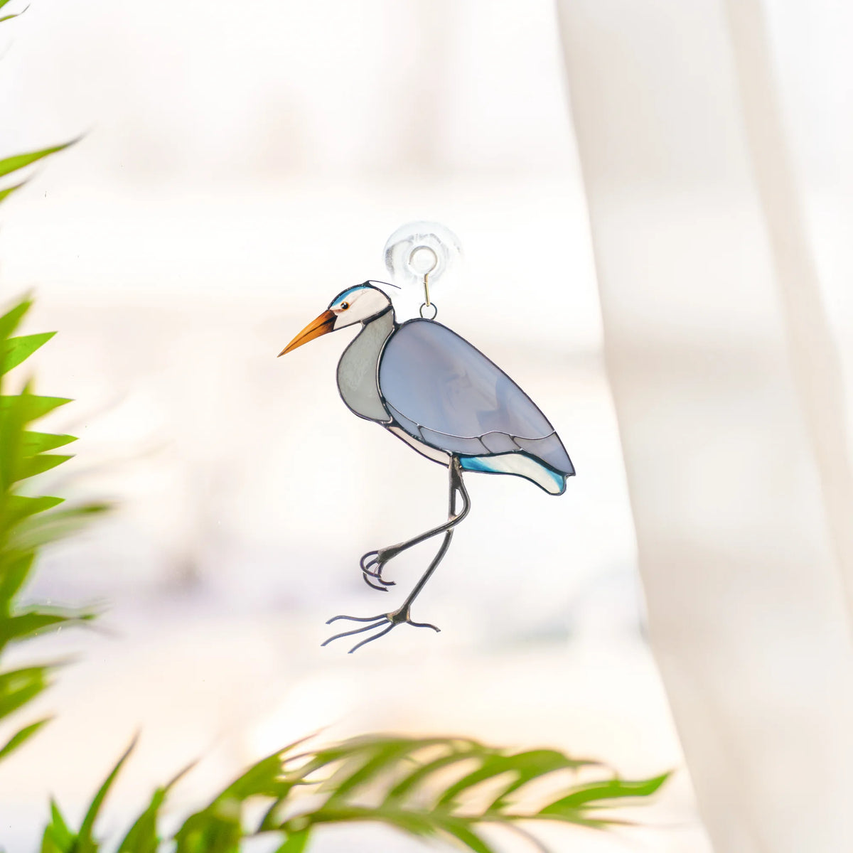 Great Blue Heron stained glass suncatcher hanging on a sunny window from a clear suction cup, palm leaves in the foreground - handmade bird window decor and a gift for bird lovers