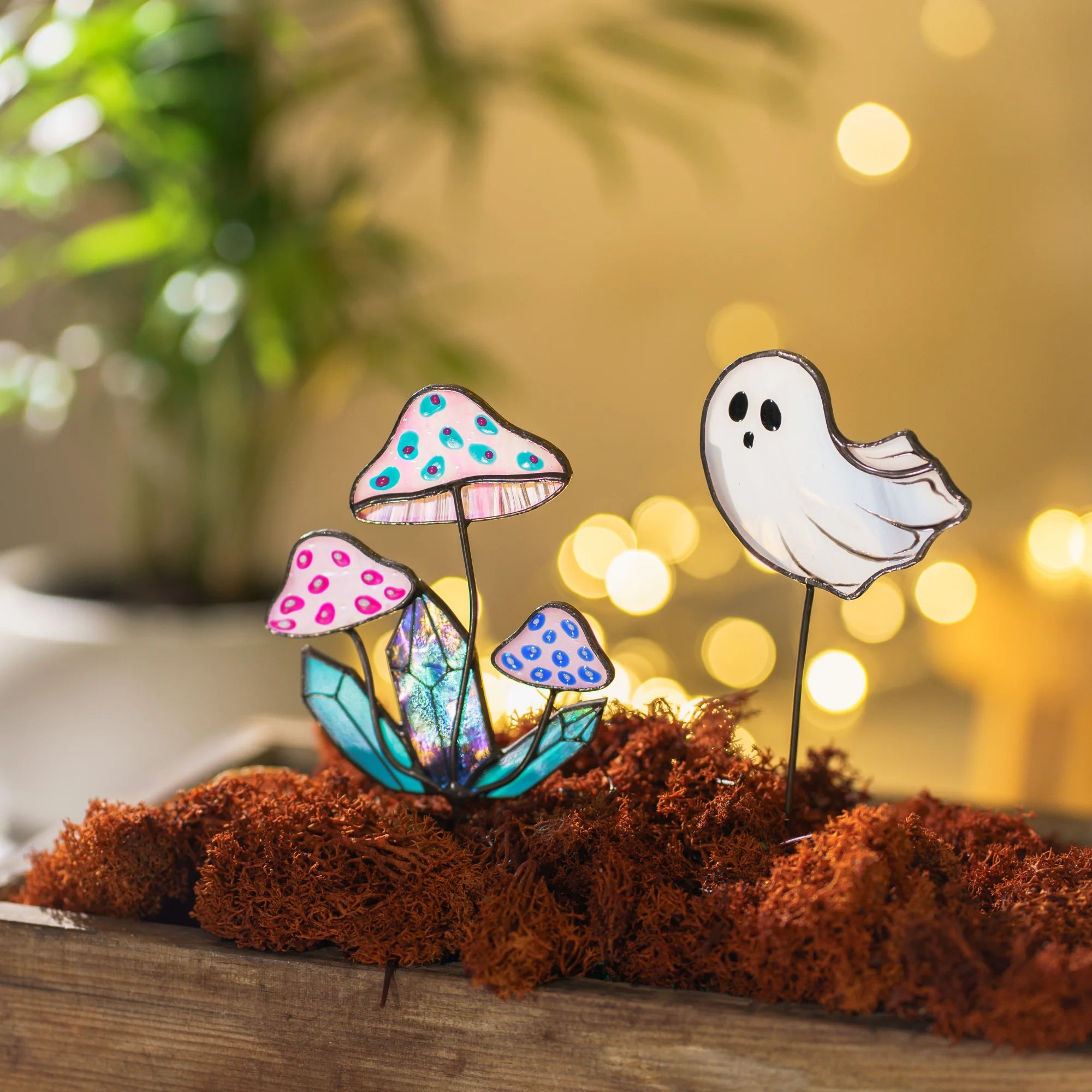 Stained glass mushrooms and ghost plant stakes lit by warm bokeh lights in a mossy wooden box - handmade cottagecore garden art and moody Halloween decor for houseplants