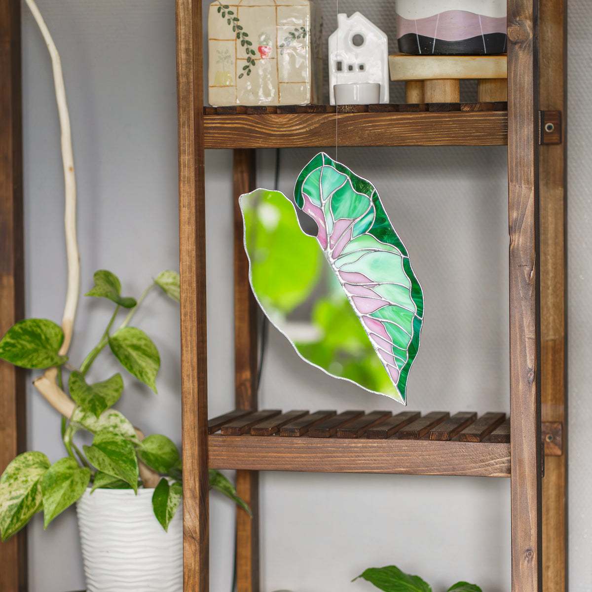 Caladium Leaf Stained Glass Mirror hanging in front of a rustic wooden shelf with pothos plants, reflecting fresh greenery - handmade stained glass wall mirror in pink and emerald green glass