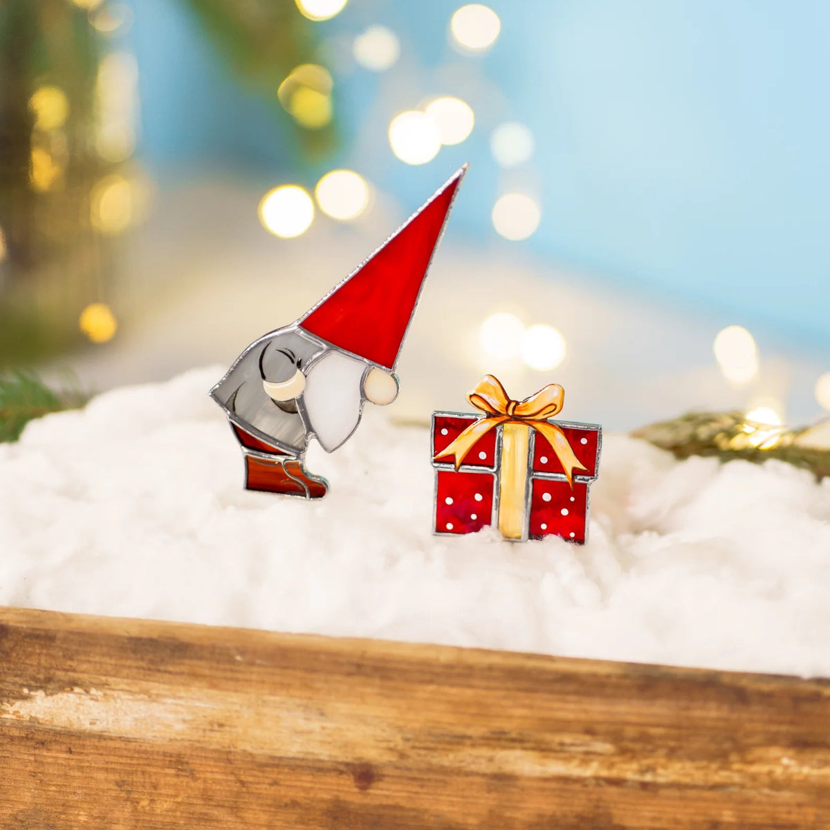 Christmas gnome with gift stained glass plant stakes standing in a wooden tray of white snow with fir sprigs and warm bokeh lights - handmade Christmas stained glass decor