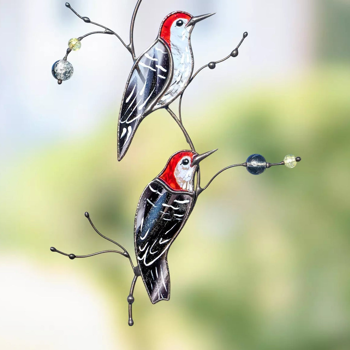A close-up view of the red-headed woodpecker suncatcher, highlighting the vibrant red glass and the decorative beads on the wire branches.