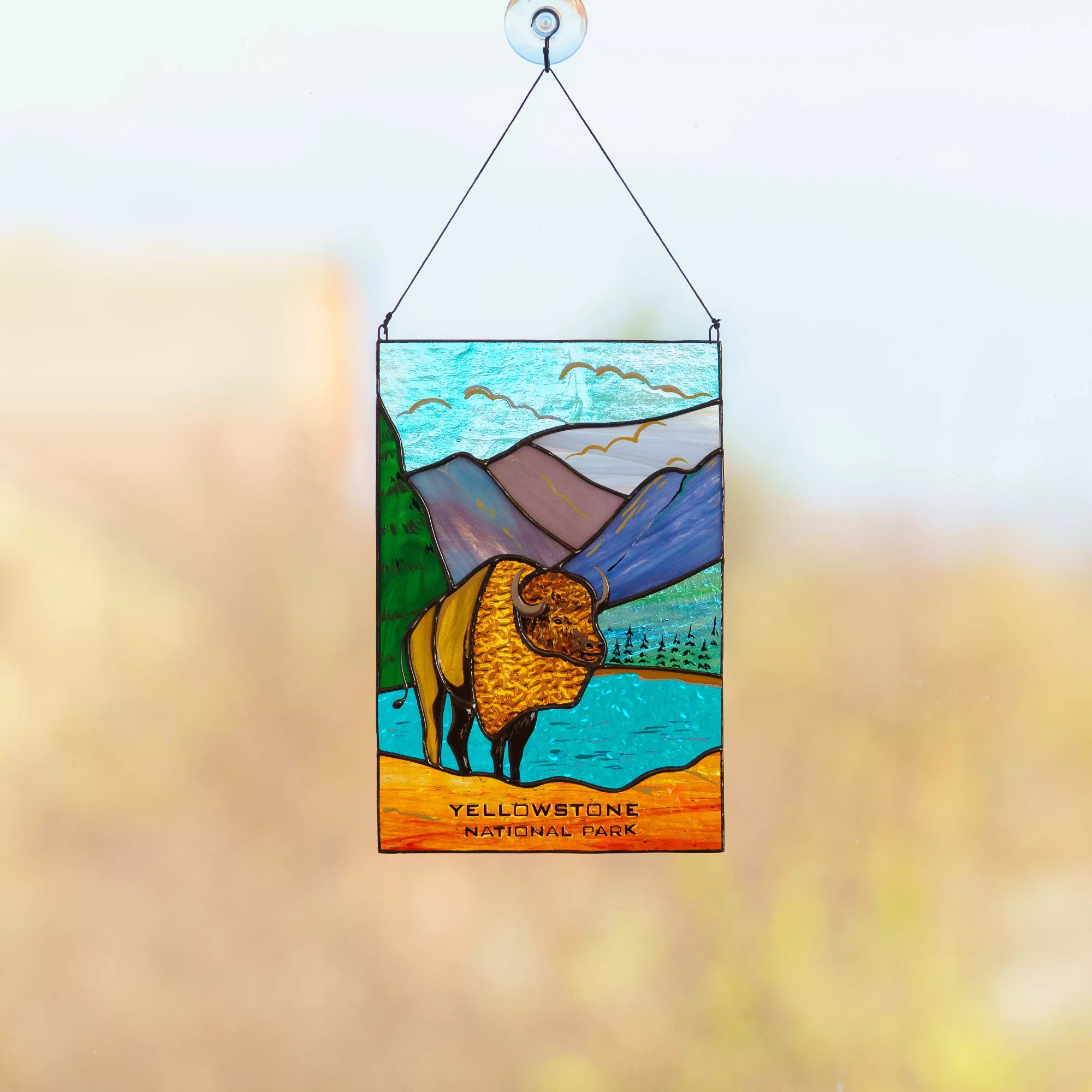 Stained glass panel of a bison in Yellowstone National Park with mountains and trees in the background.