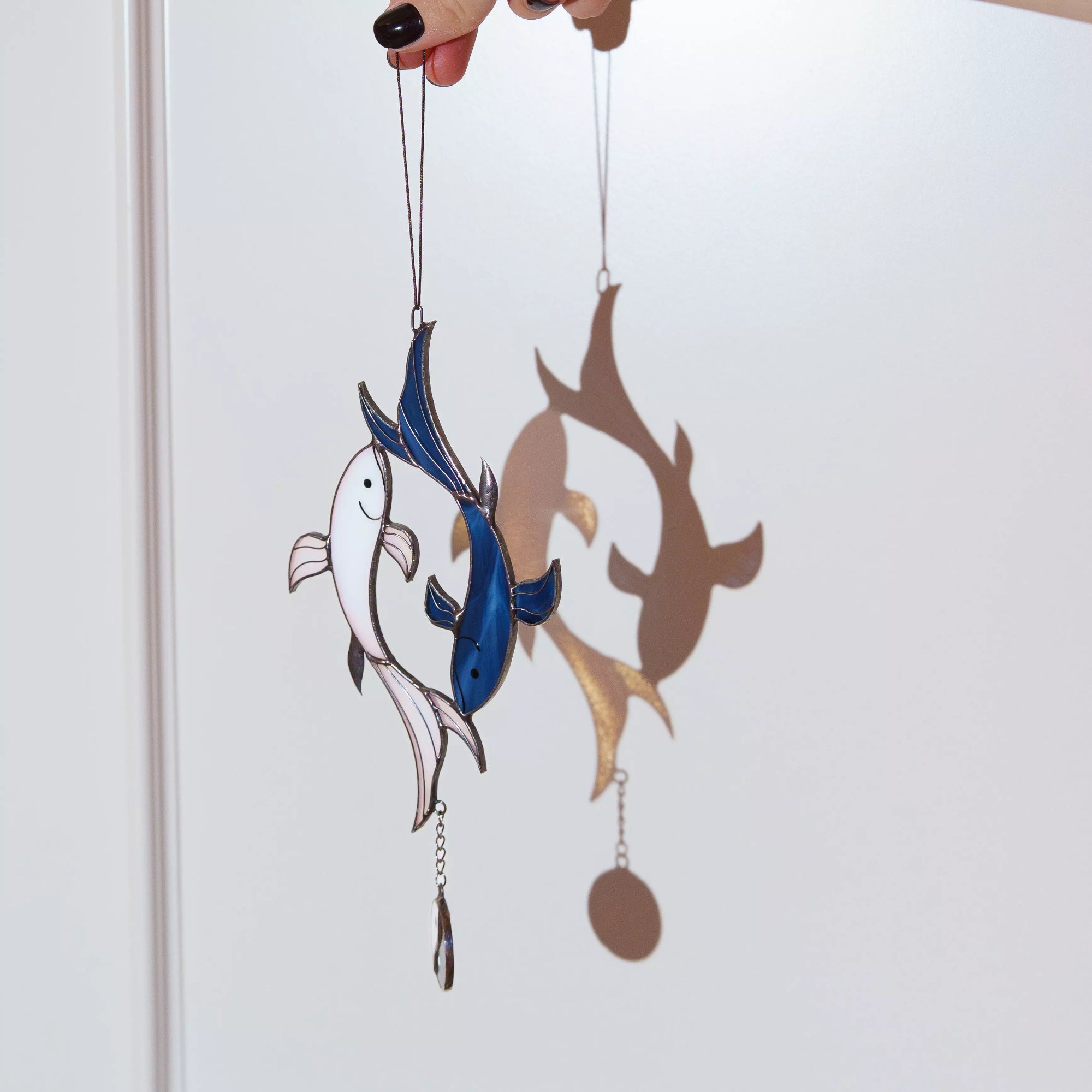 Stained glass fish window hanging with a white, blue, and brown design on a plain background.