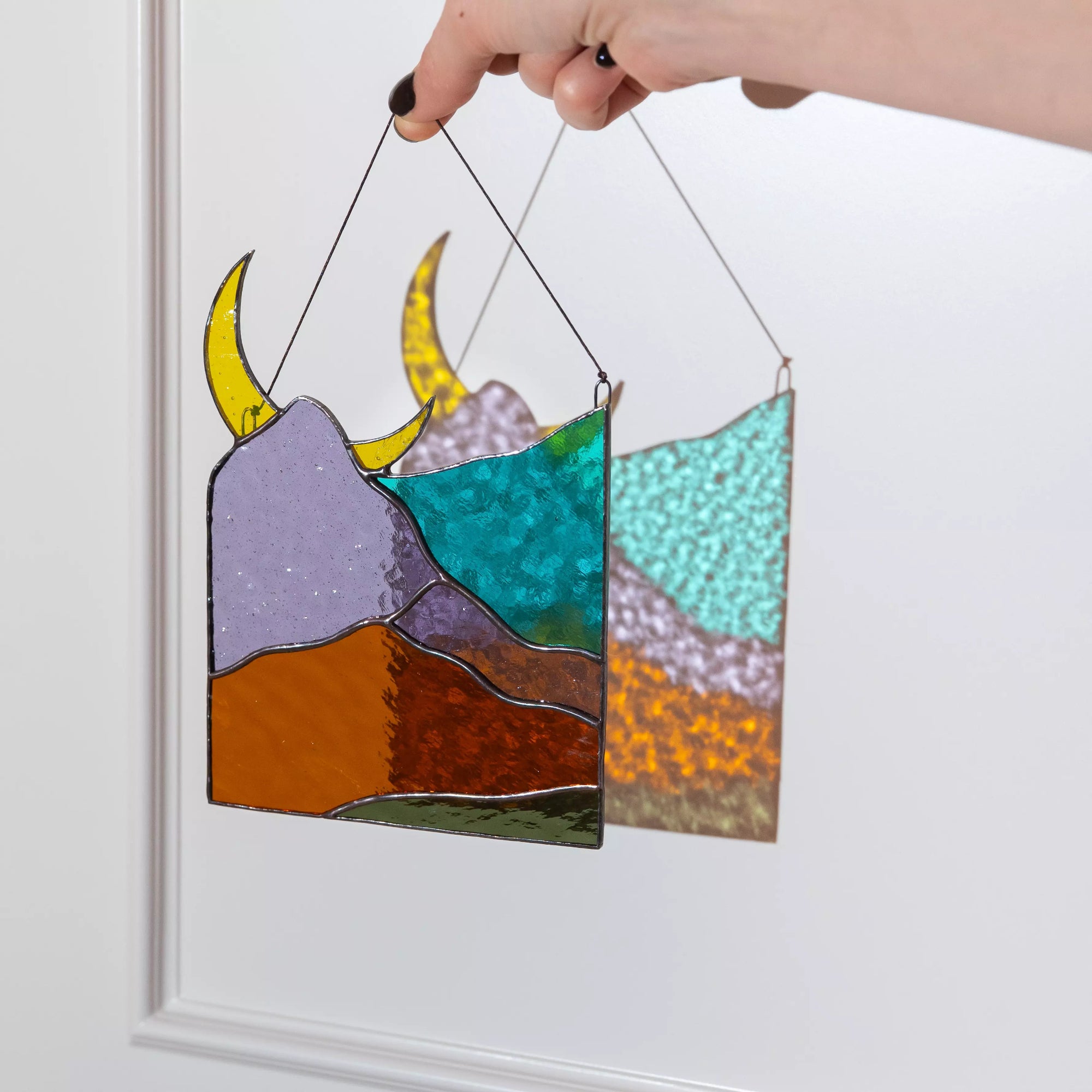Hand holding a stained glass panel with mountain and moon design against a white background