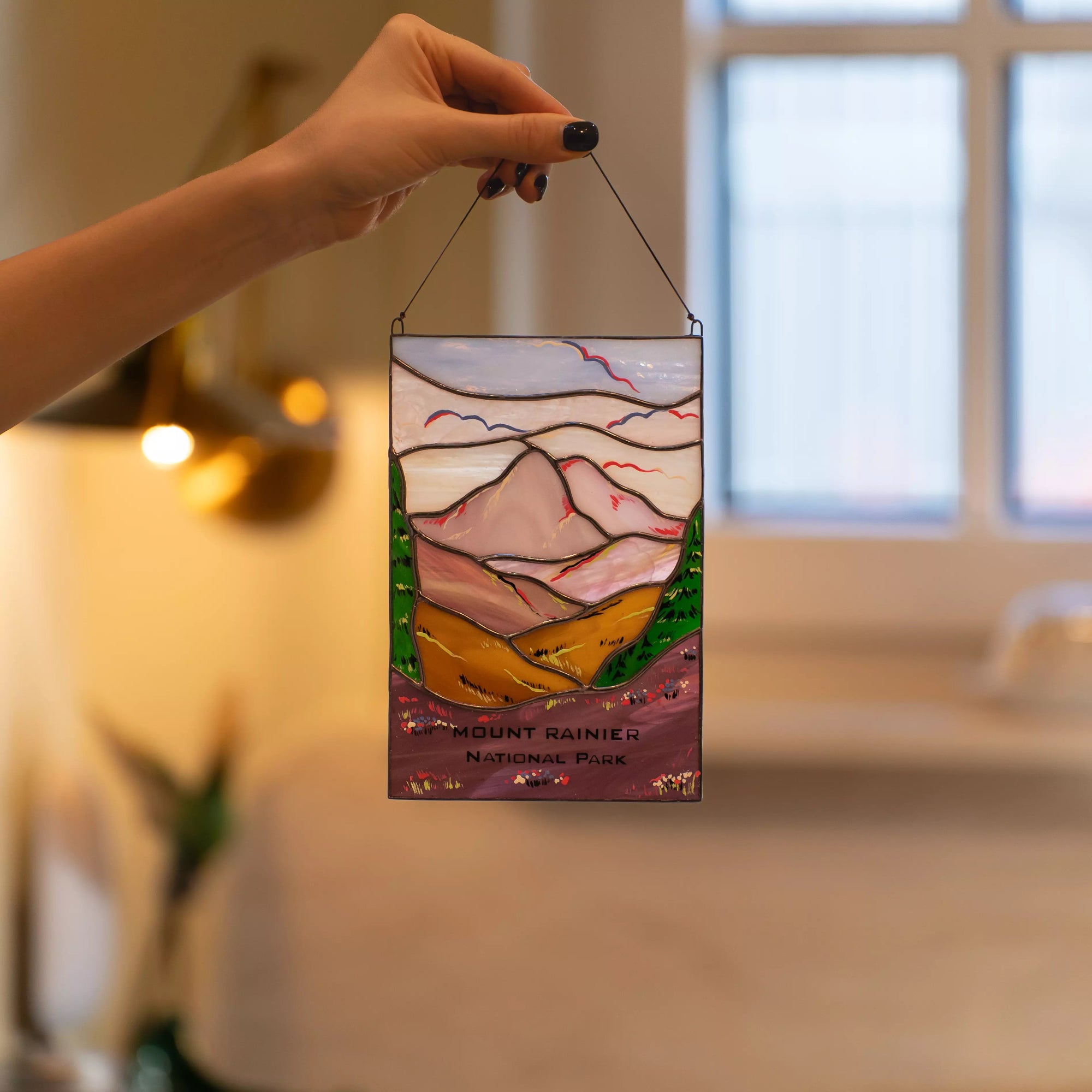 Hand holding a stained glass panel of Mount Rainier with a blurred indoor background