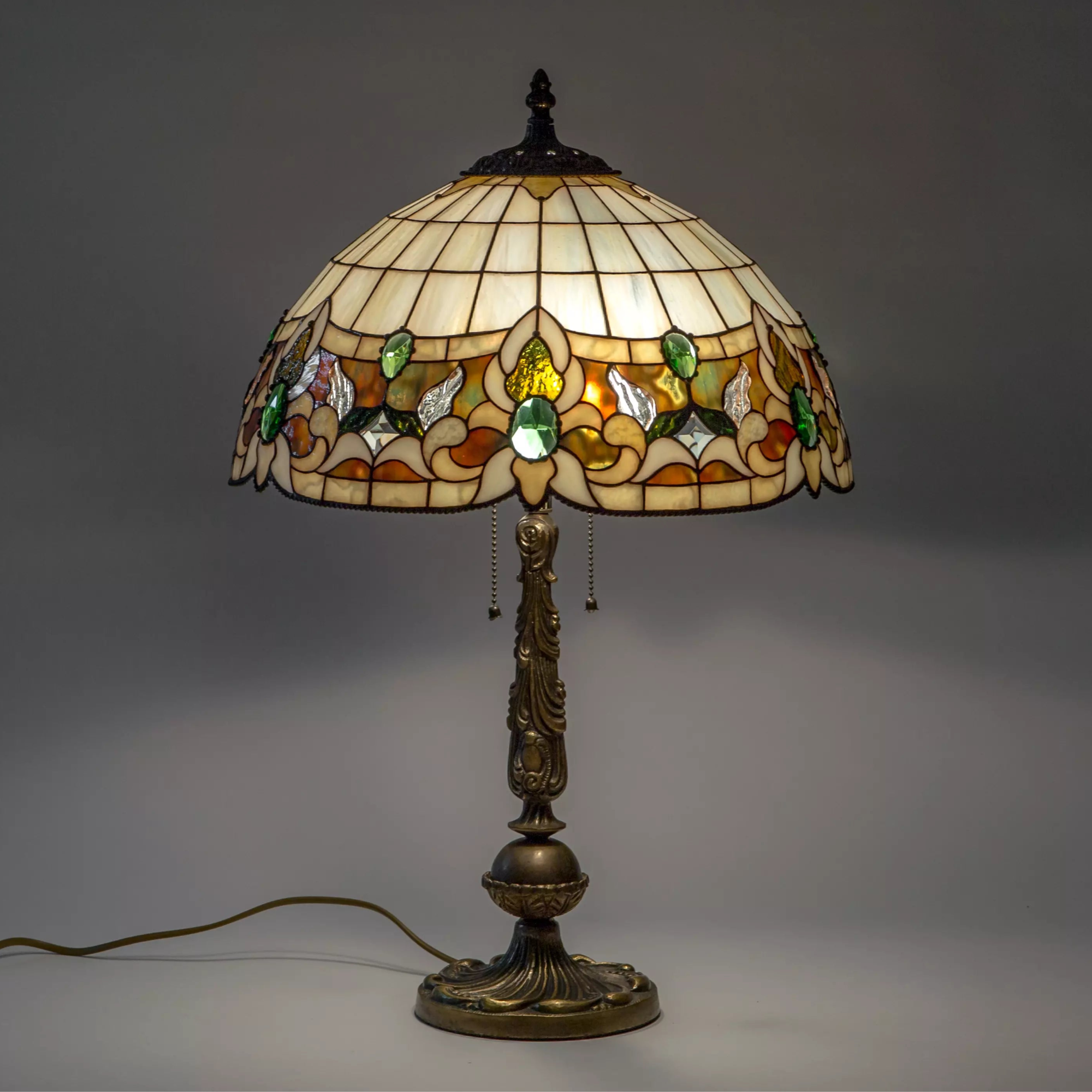 Tiffany-style table lamp with stained glass shade in green tones and ornate bronze-tone base