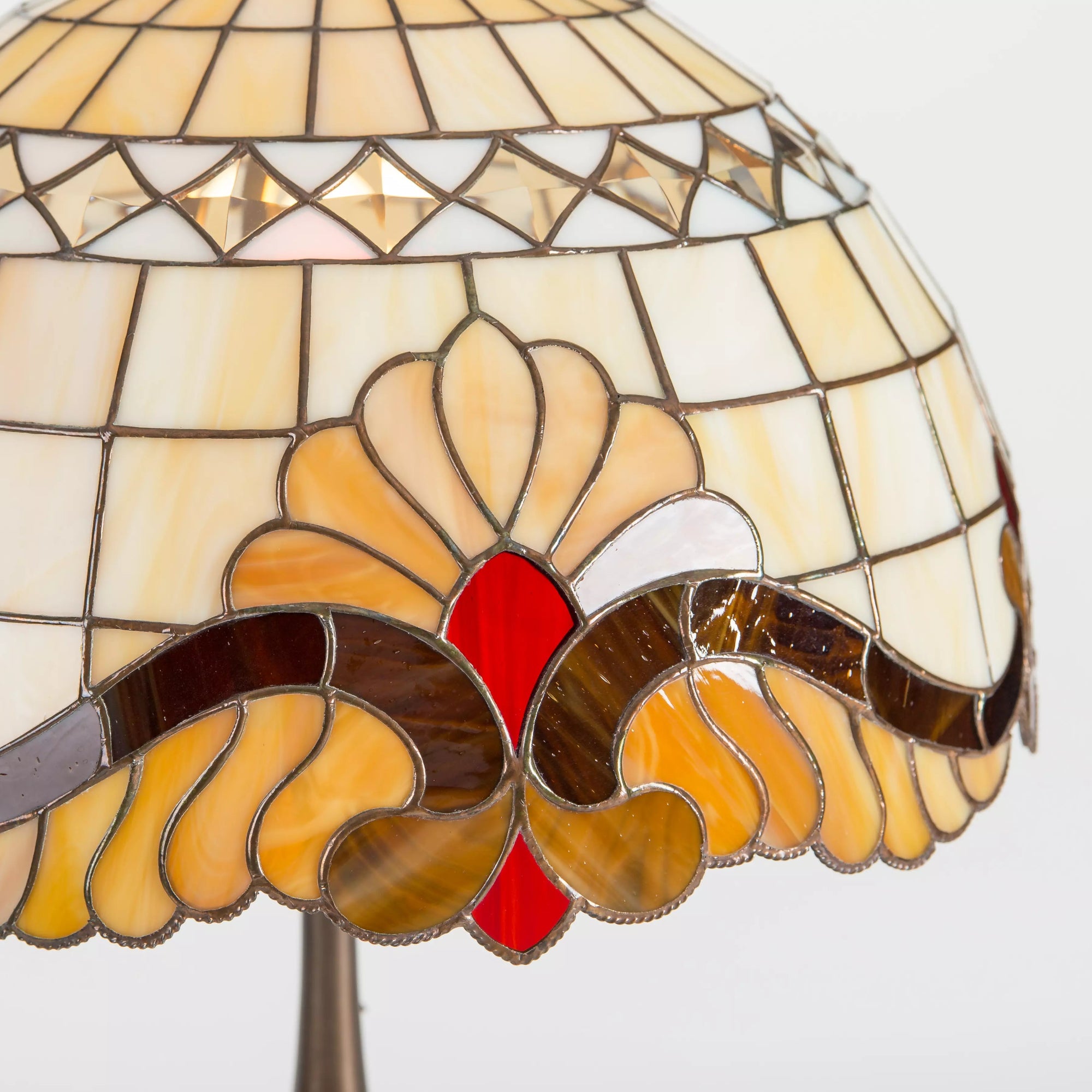 Stained glass lamp close-up showing red jewel, amber petals, and brown scrolls