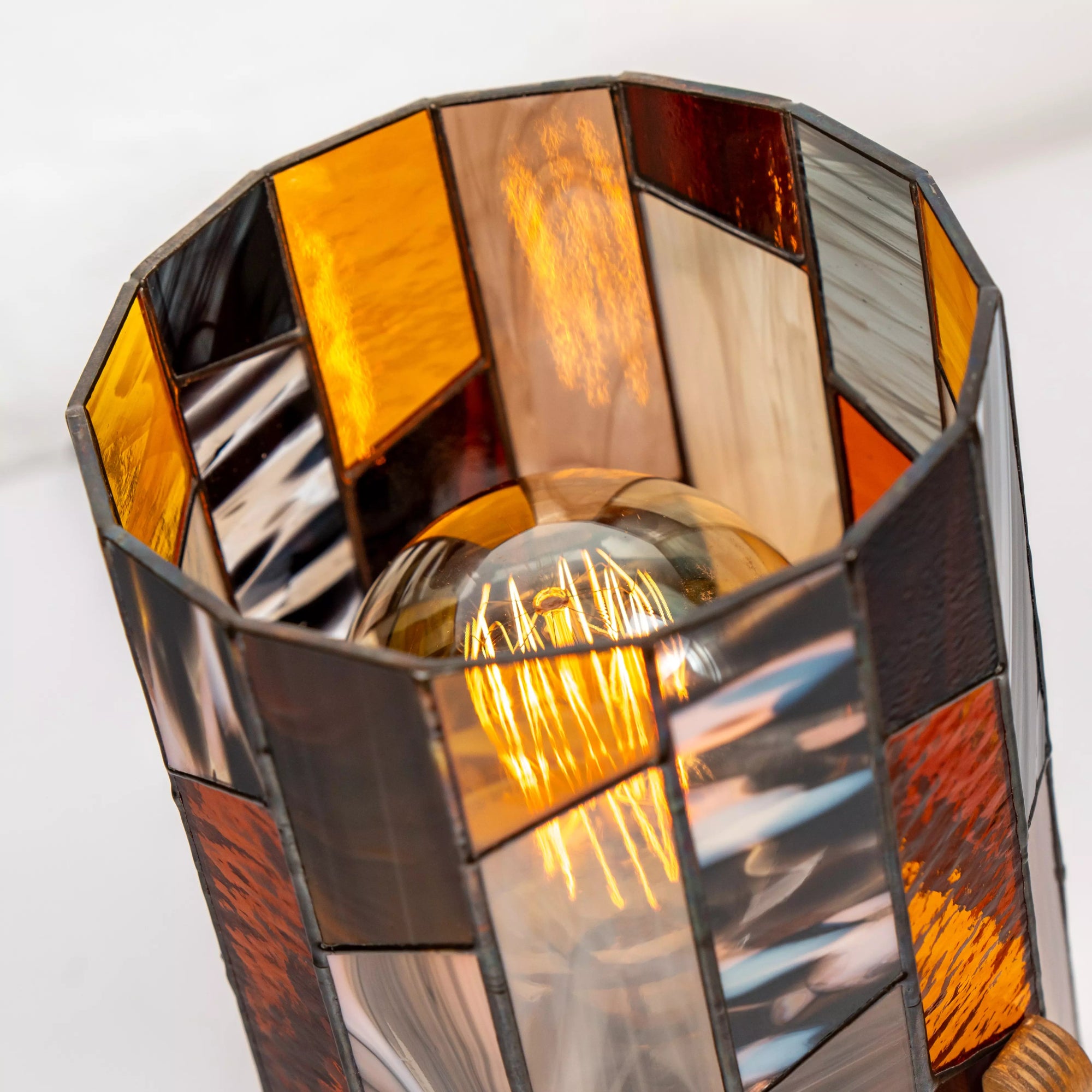 Top view of stained glass lamp with Edison bulb, amber and brown glass panels creating a glowing geometric pattern.