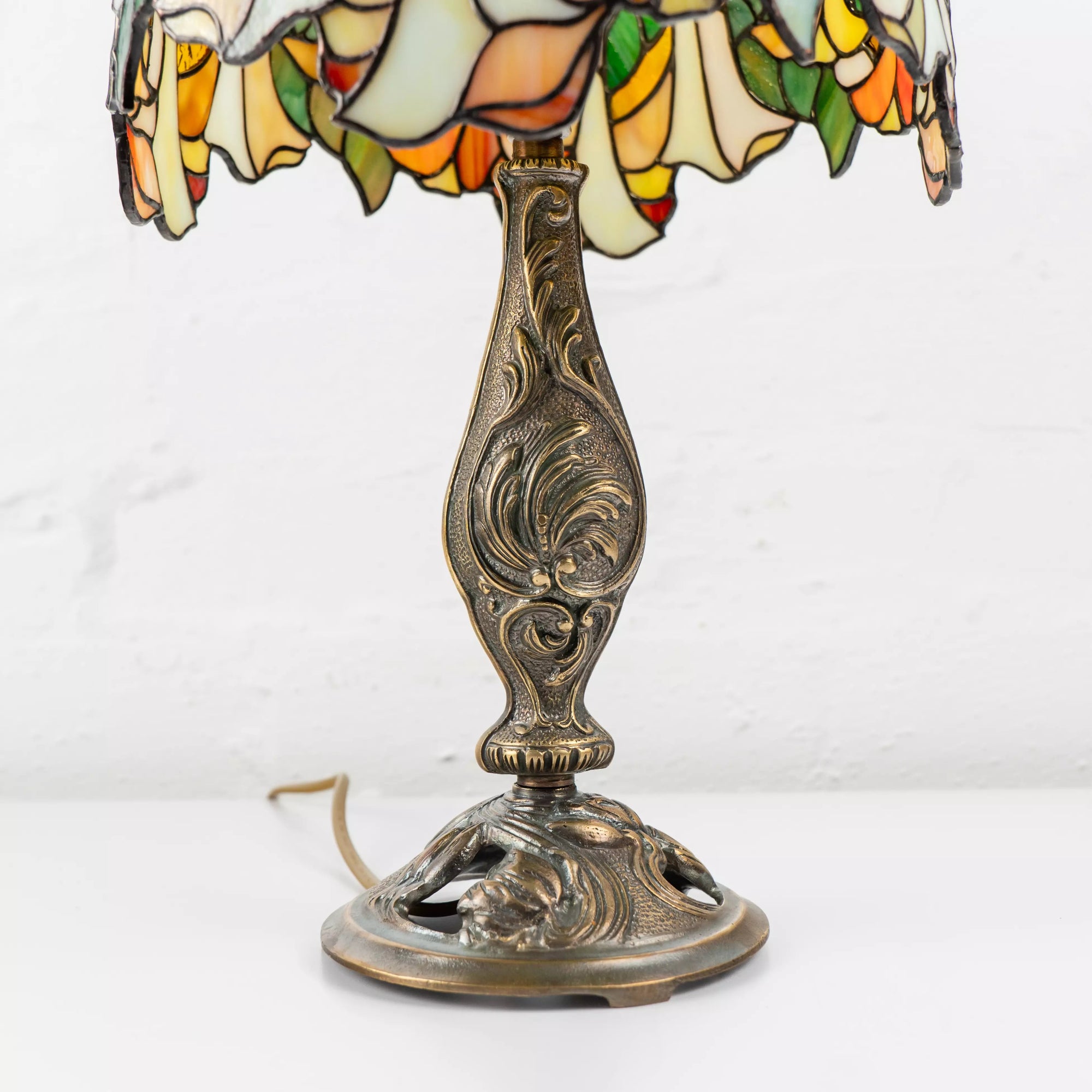Close-up of antique bronze lamp base with floral engravings supporting colorful stained glass shade.