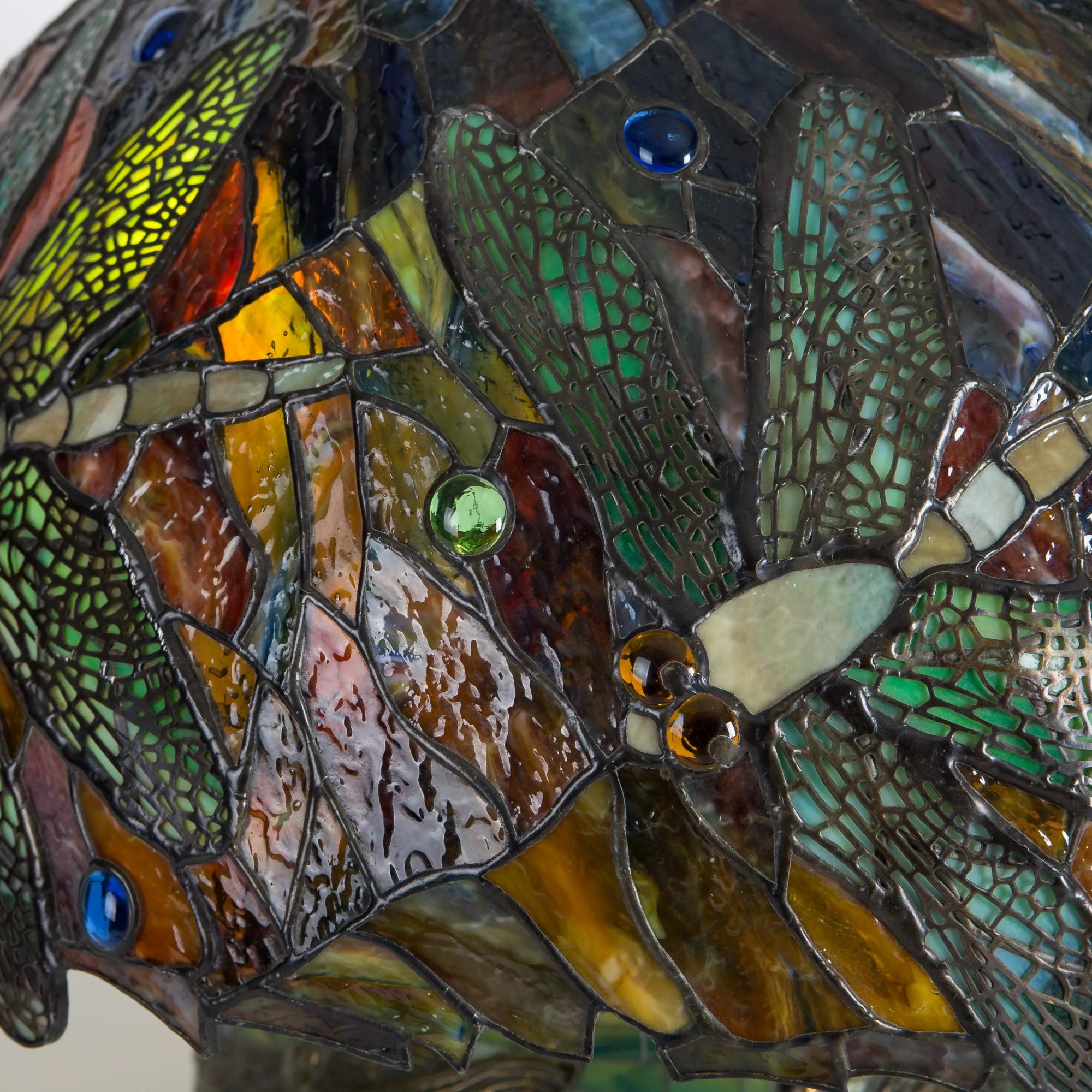 Close-up showing overlapping dragonfly wings with red, amber, green, and jewel-toned stained glass