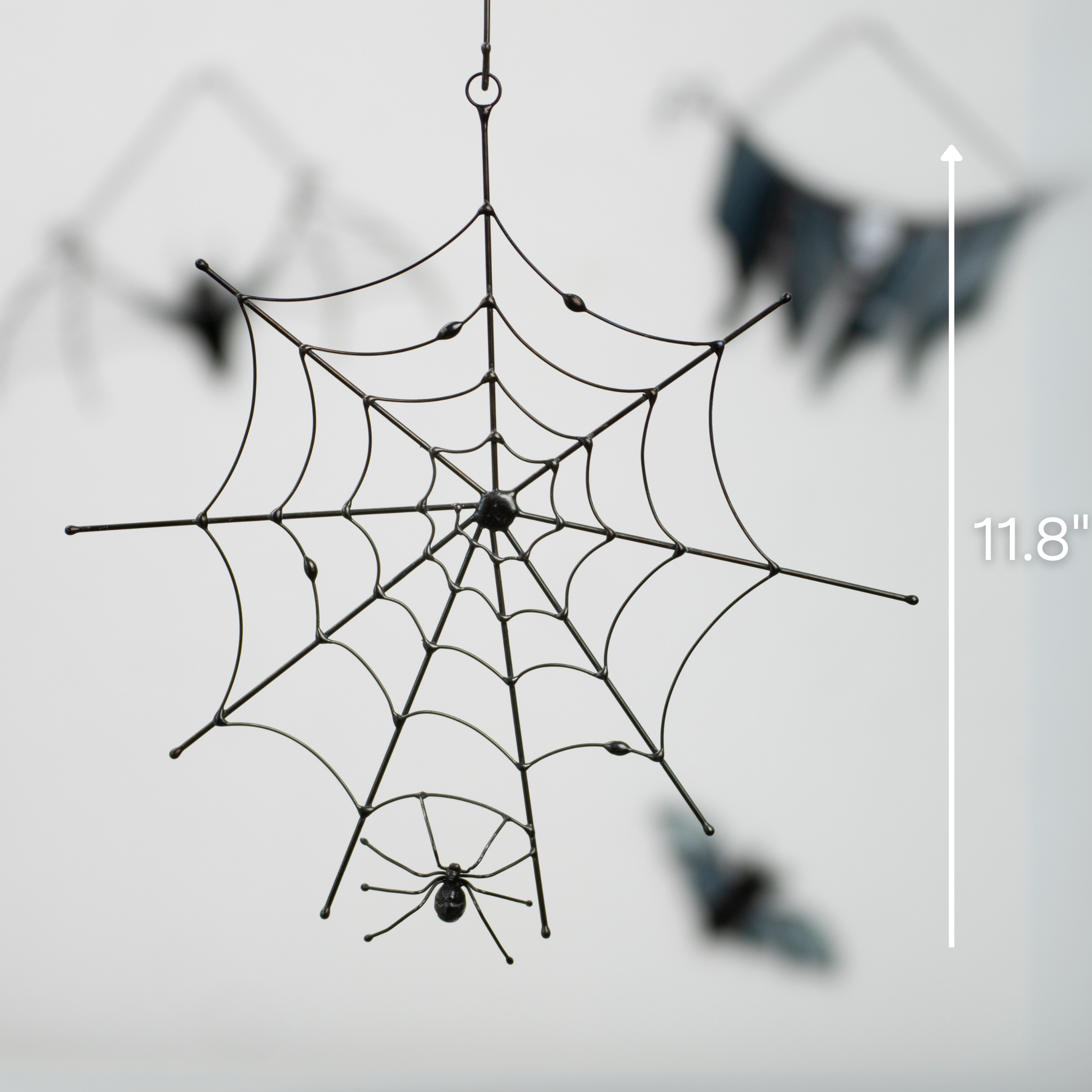 Spider web suncatcher shown hanging in front of a neutral wall with size marker at 11.8 inches, surrounded by other bat decorations.