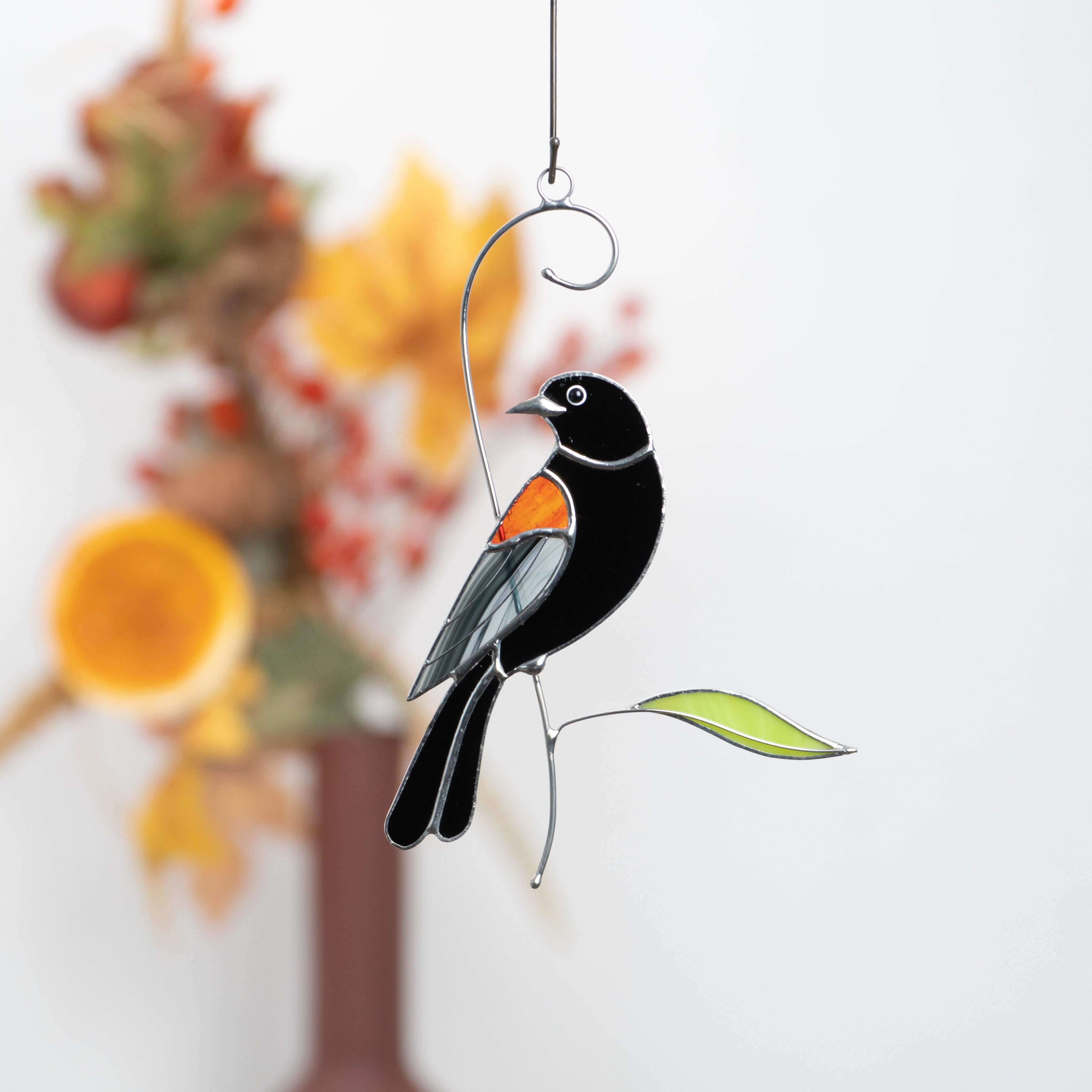 Stained glass blackbird hanging against autumn-themed background with warm colors.
