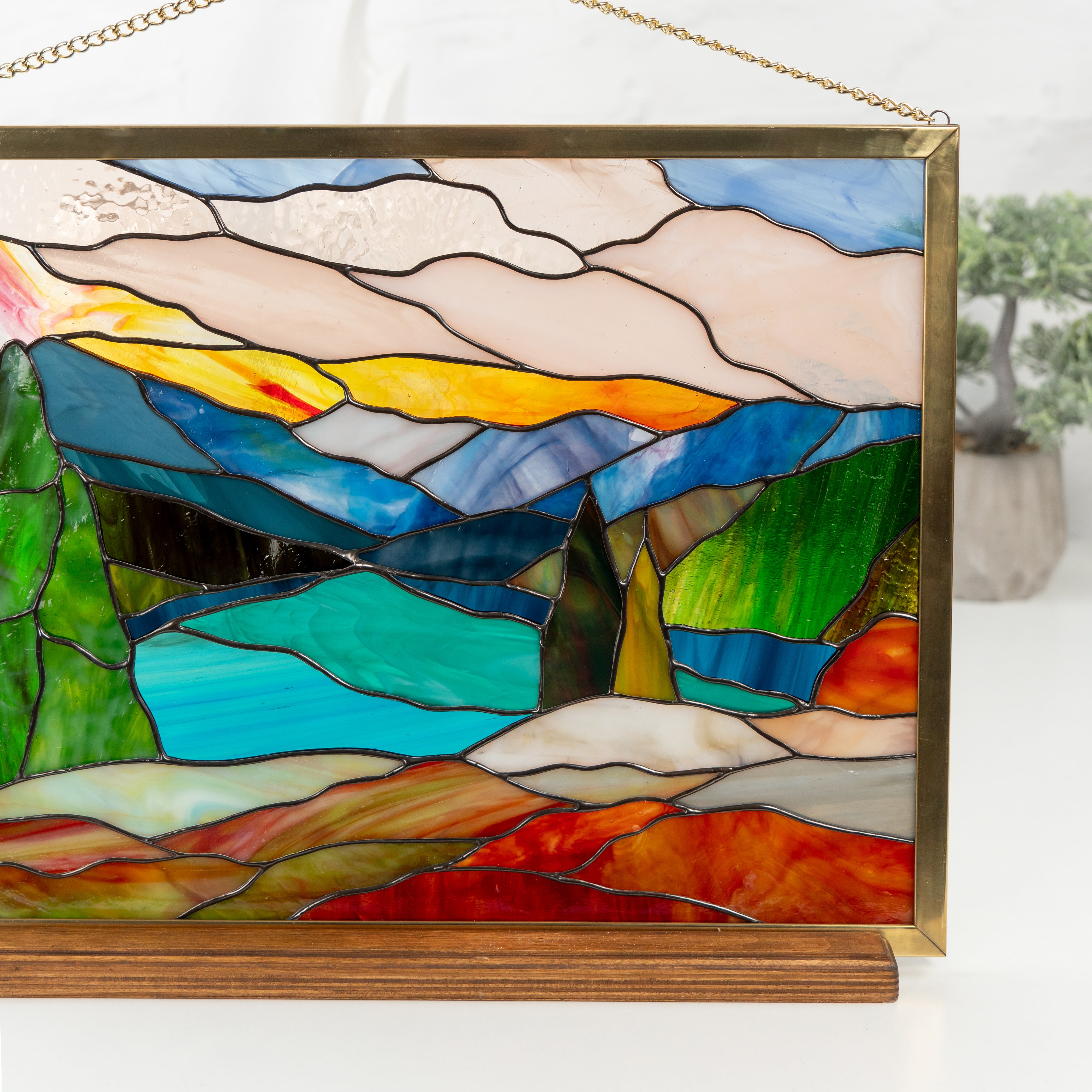 Stained glass artwork showing Mount Rainier landscape with lake, trees, and sunset, displayed on wood base indoors