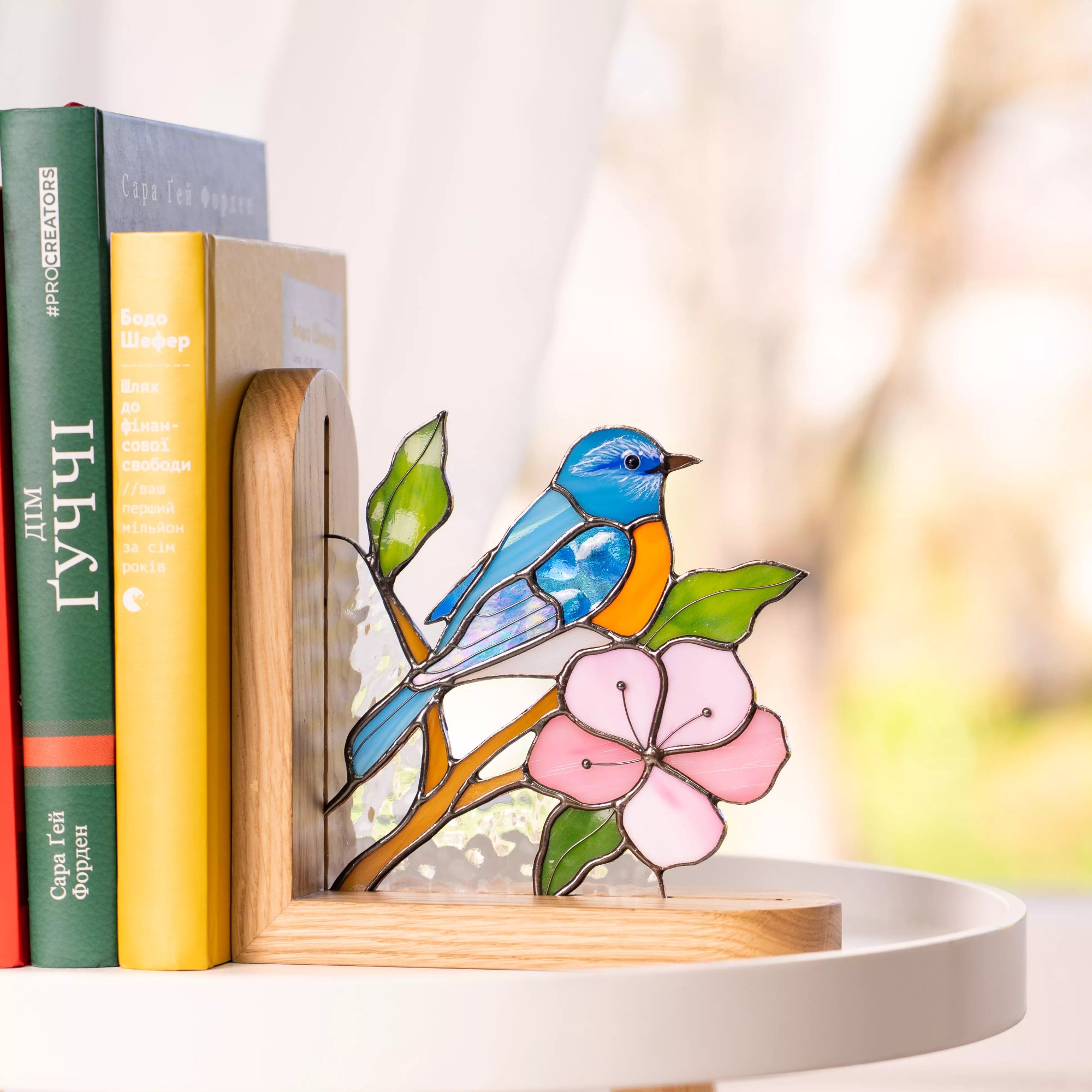 Handmade blue bird stained glass bookend displayed on a round table with books.