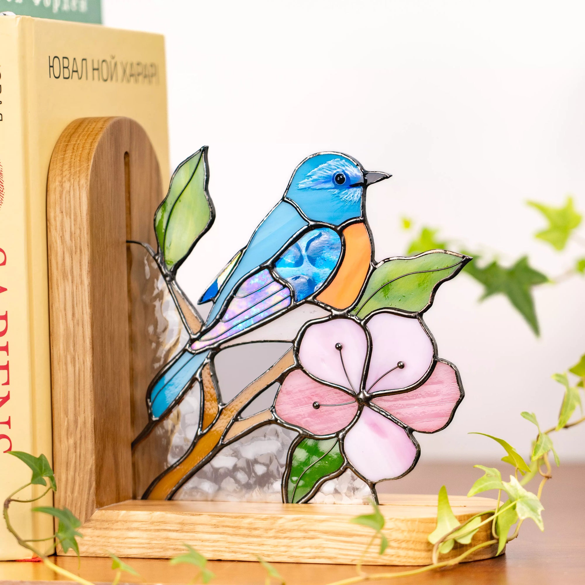 Blue bird stained glass bookend holding books upright on a wooden shelf.