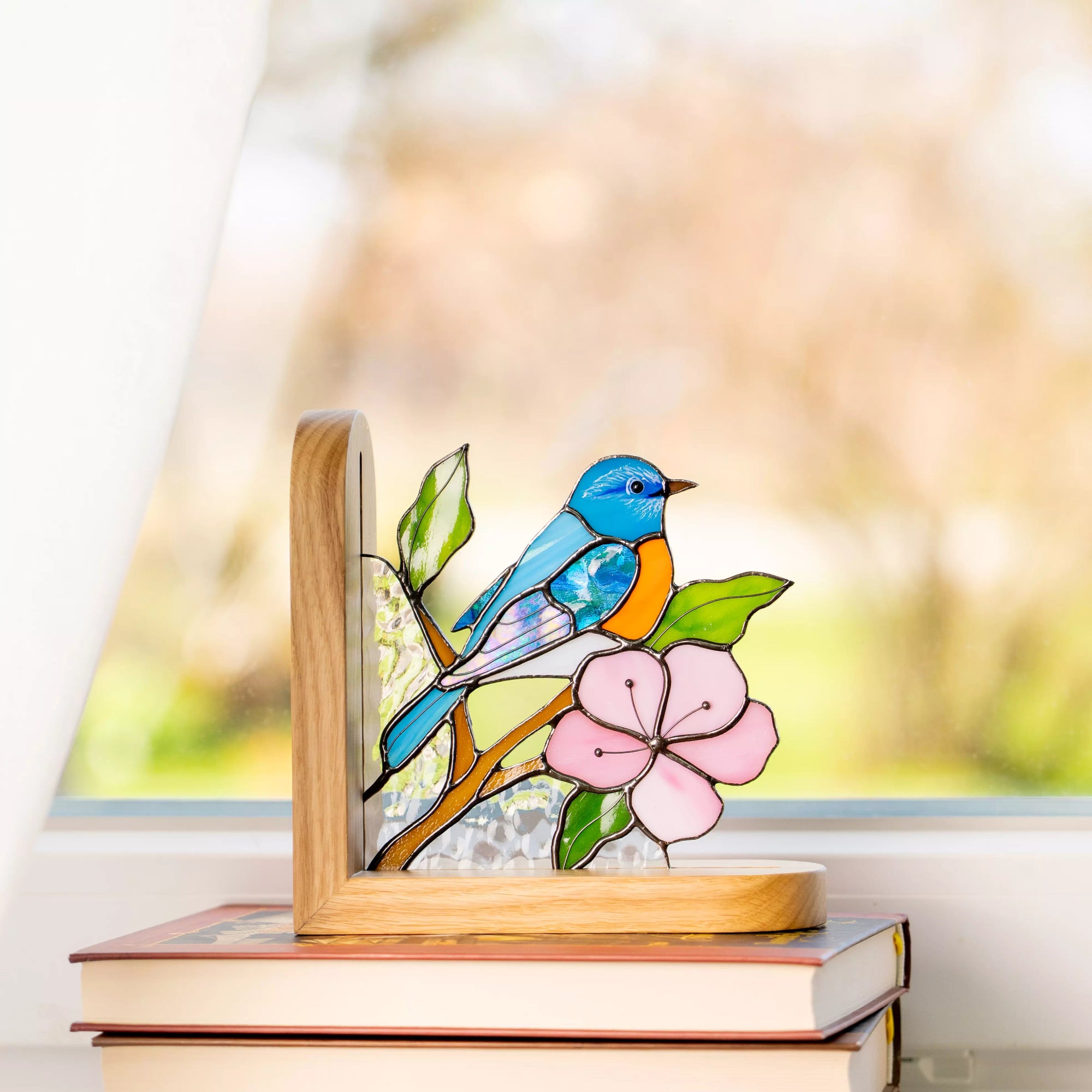 Blue bird stained glass bookend placed near a window in a wooden base.