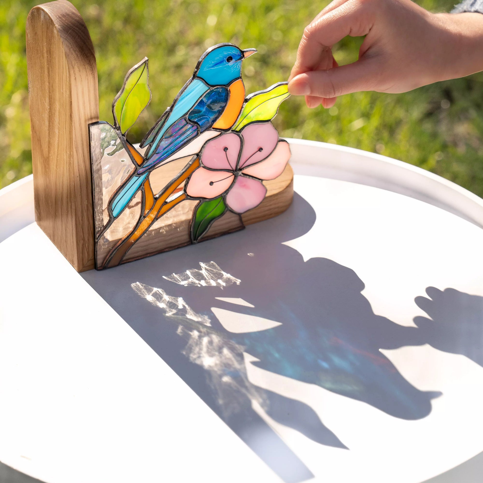 Blue bird stained glass panel photographed outdoors in sunlight, casting colorful reflections and shadows on the surface.