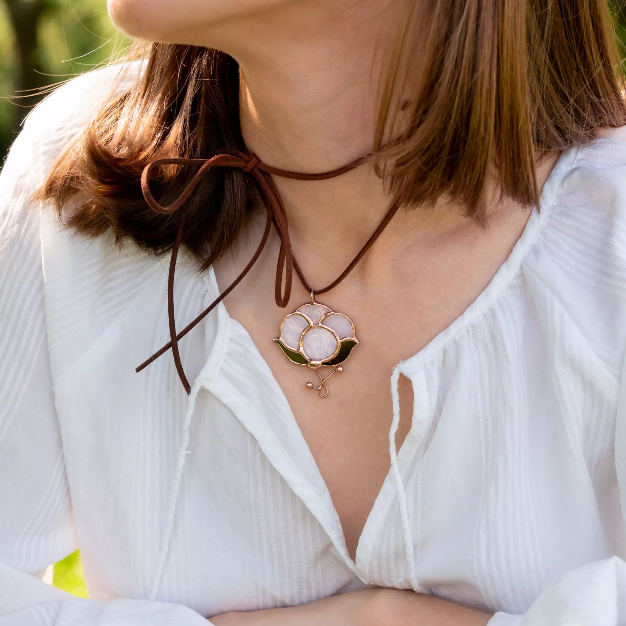 Woman in white blouse wearing brown suede cord cotton glass pendant while sitting outdoors