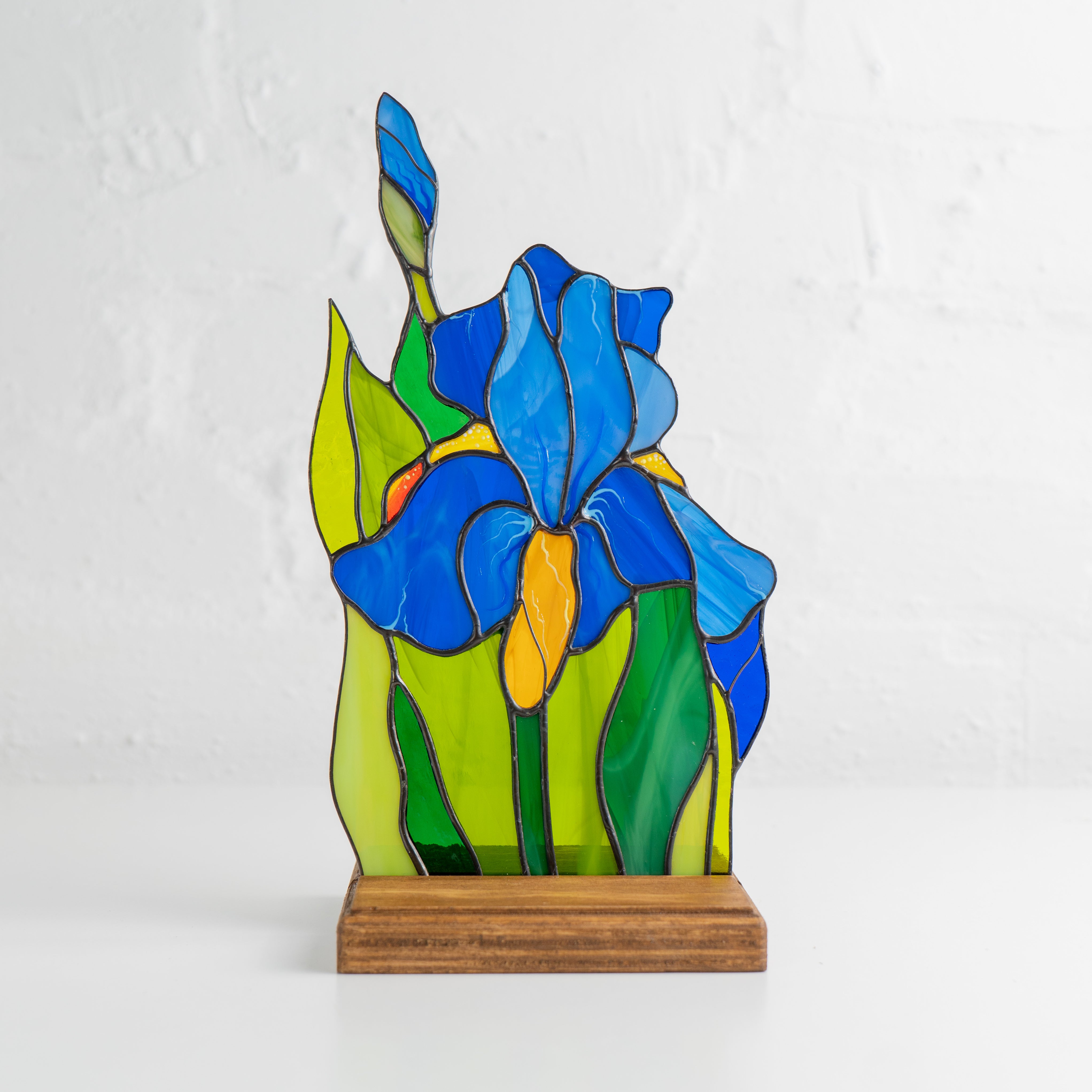 Stained glass iris flower panel in wooden stand, placed against a white background.