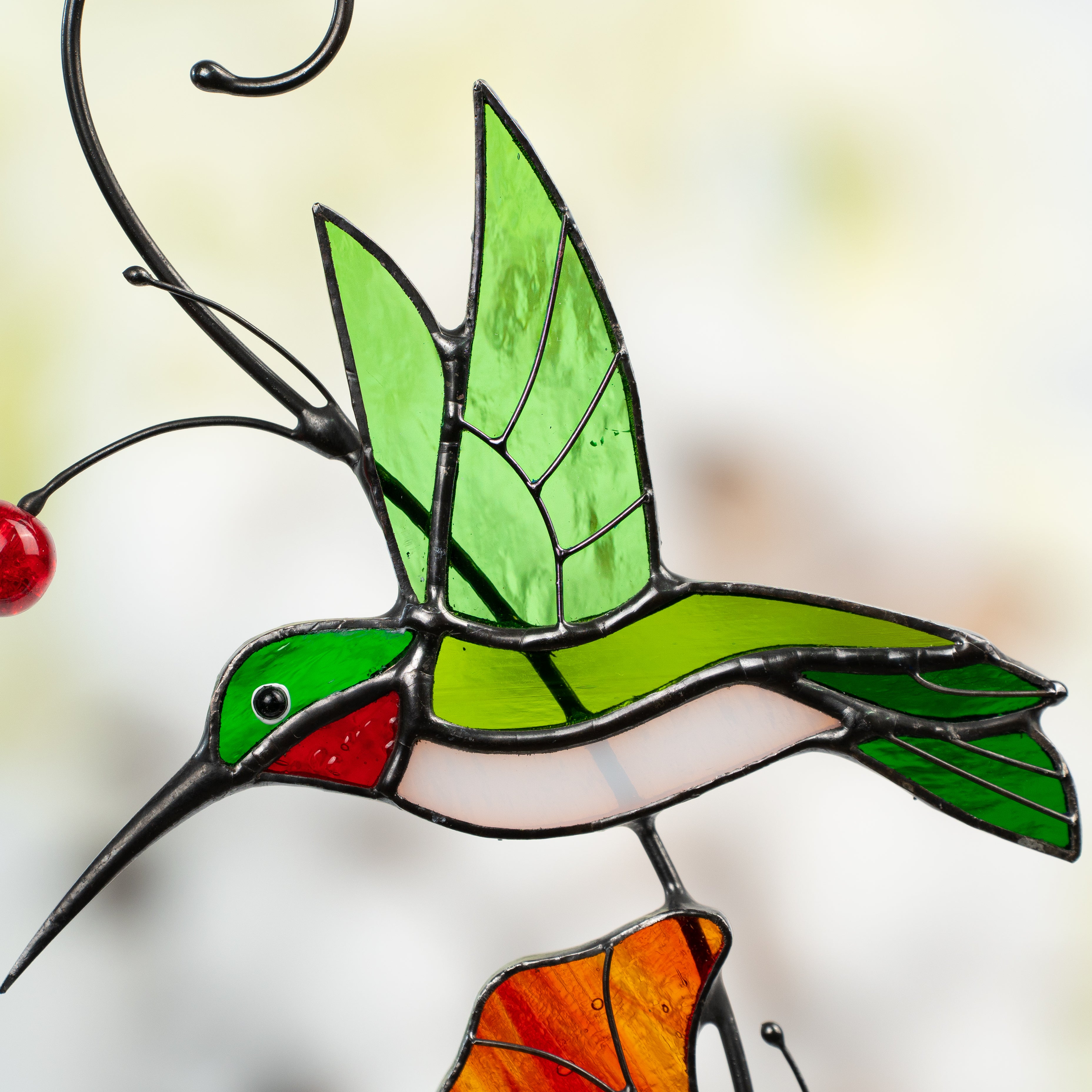 Close-up of green and red stained glass hummingbird in flight with detailed wing structure