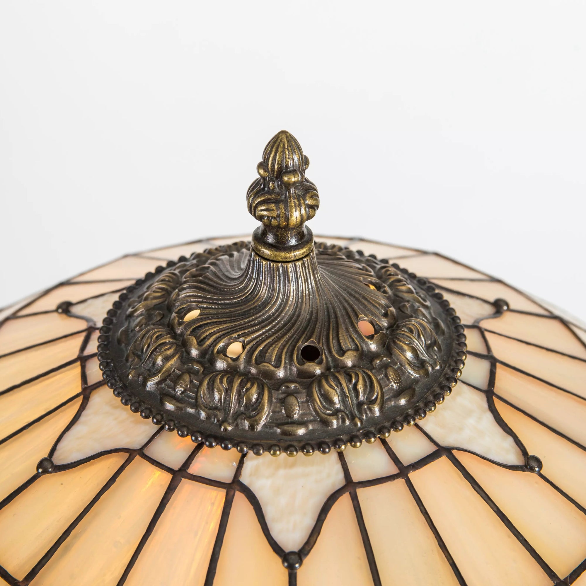 Closeup of ornate bronze-tone finial and textured glass panels on Tiffany-style lamp