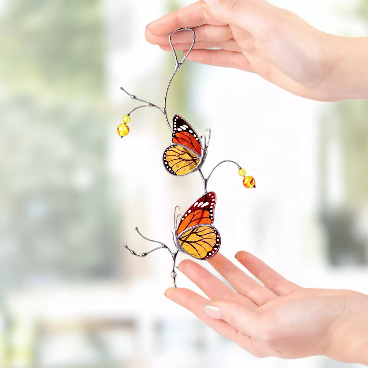 Stained glass monarch butterfly suncatcher held by a hand with a blurred background