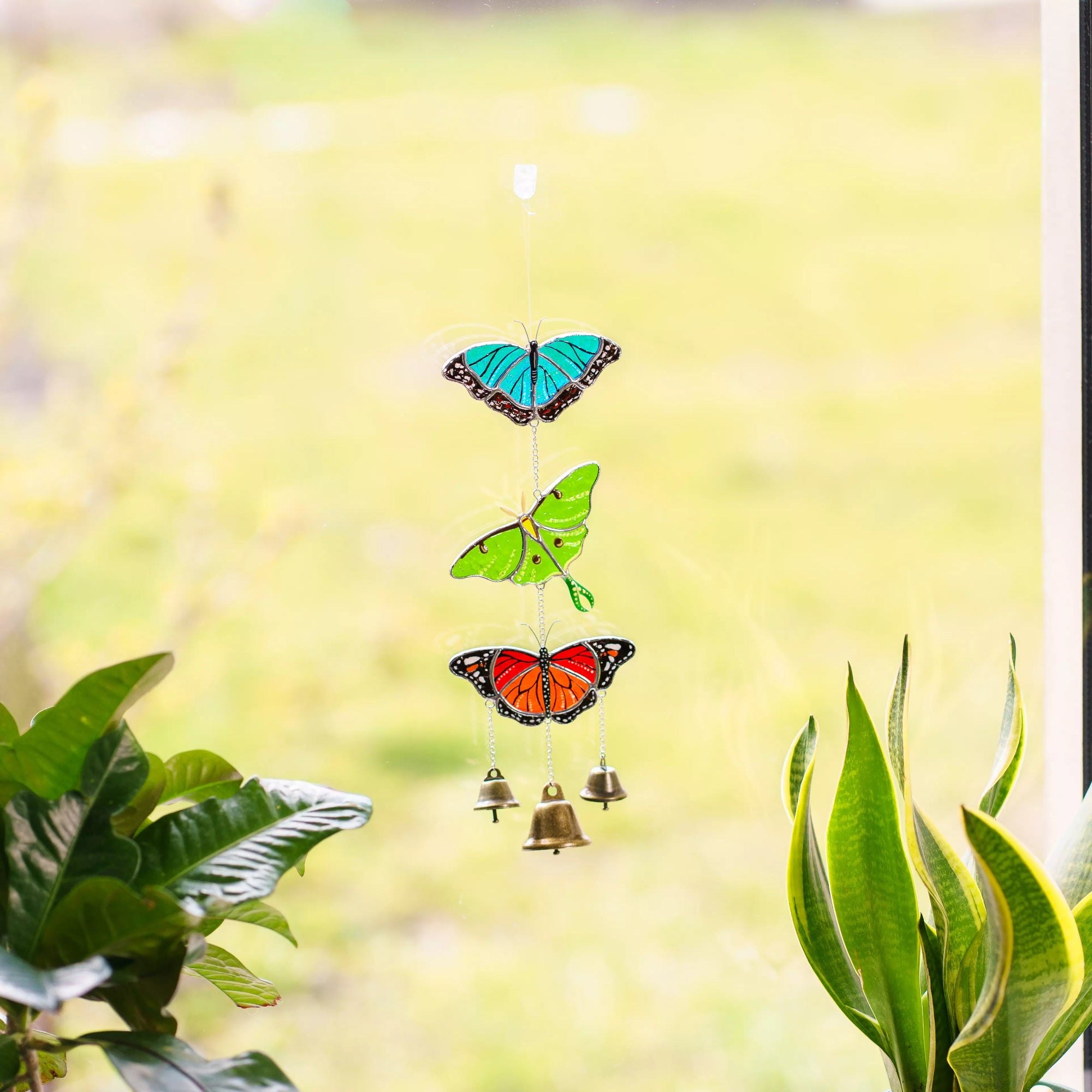Stained glass butterfly-shaped wind chime with bells against a blurred green background