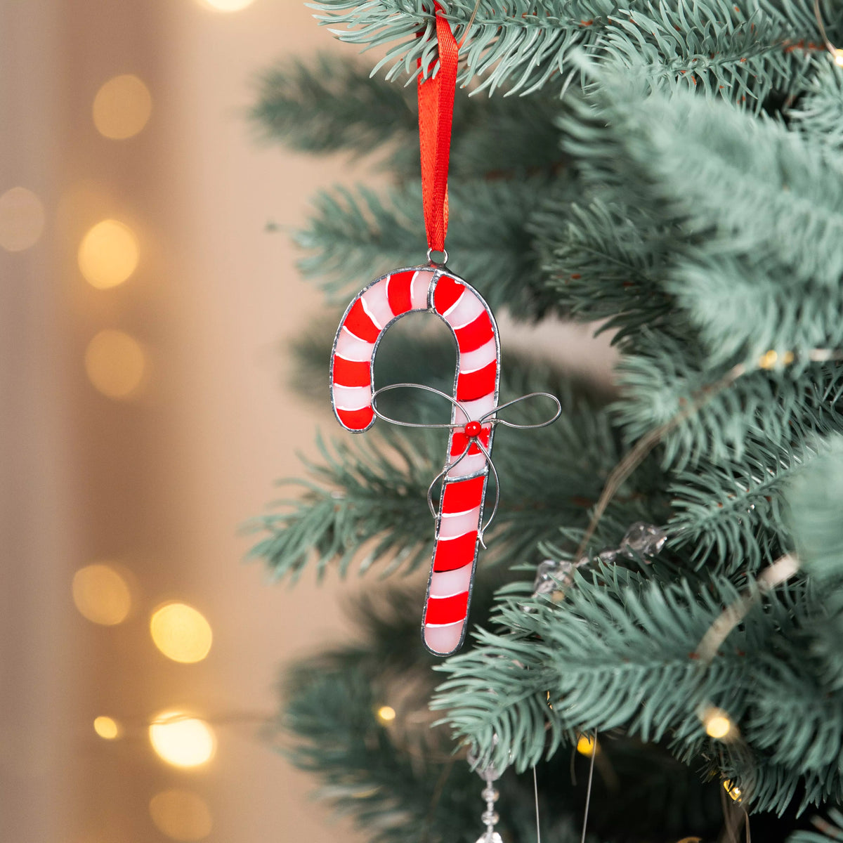 Candy cane stained glass suncatcher hanging on a Christmas tree with blurred lights in the background