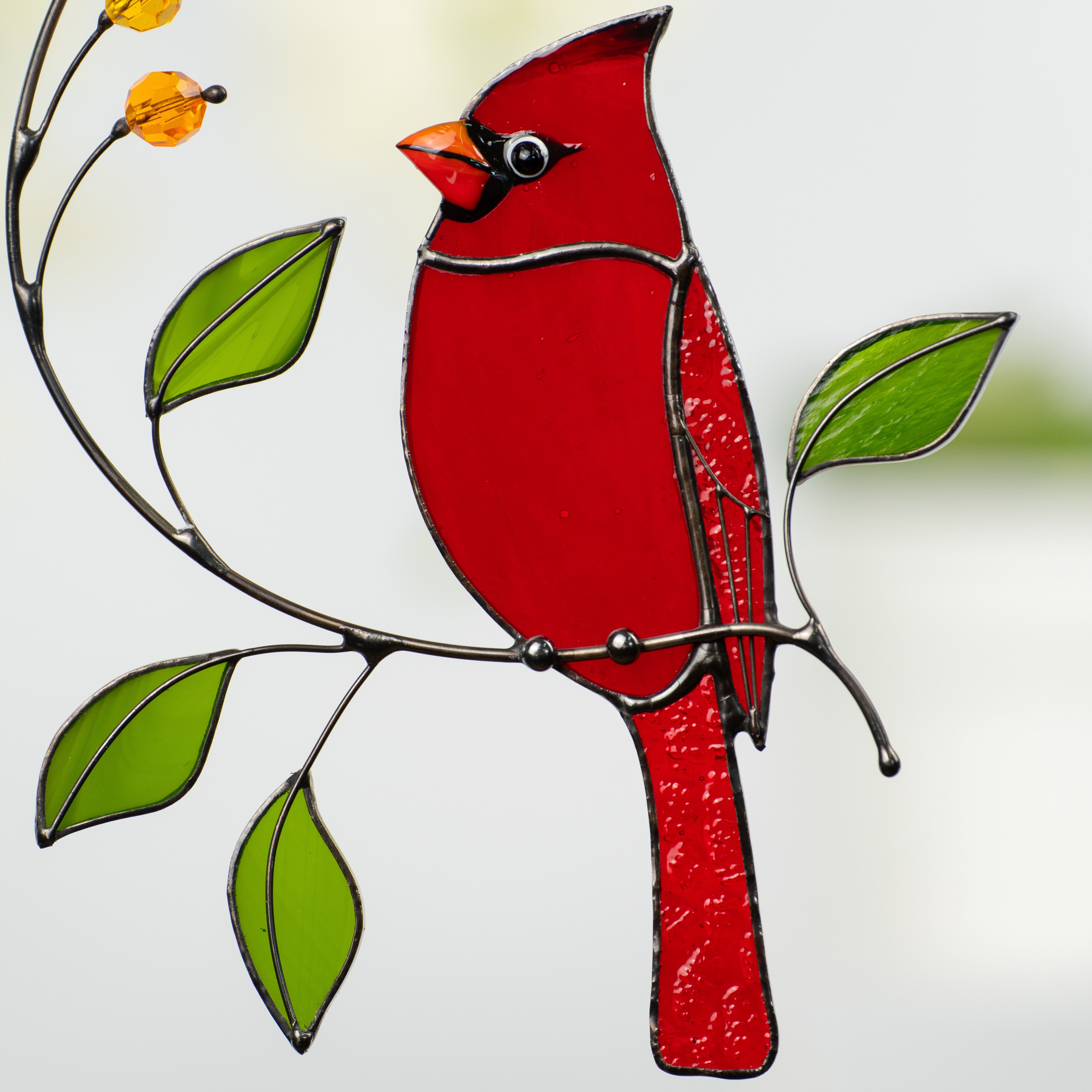 Close-up of stained glass red cardinal sitting on a curved branch with green glass leaves.