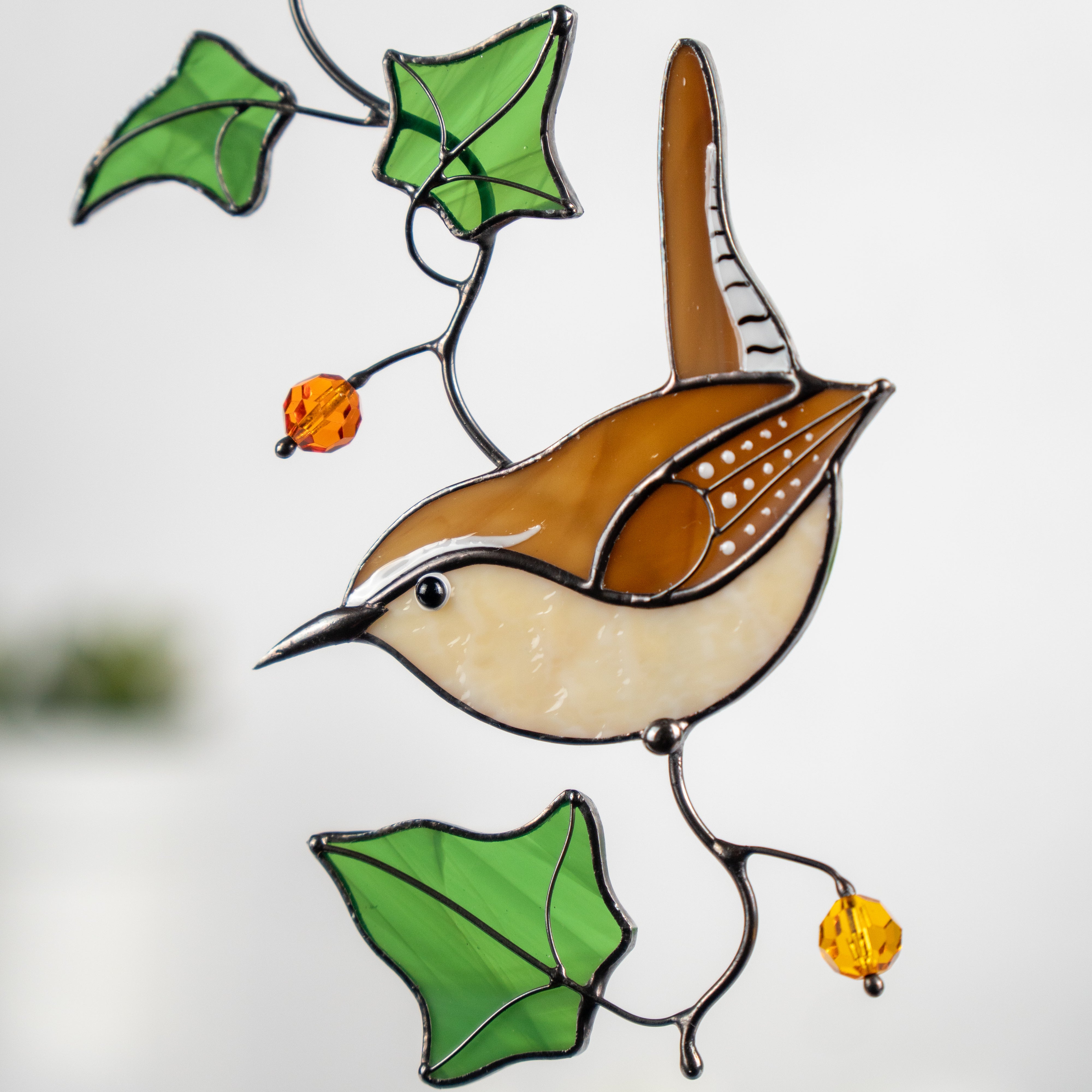 Close-up of Carolina wren stained glass suncatcher, featuring amber and cream glass body, green ivy leaves, and orange beads.