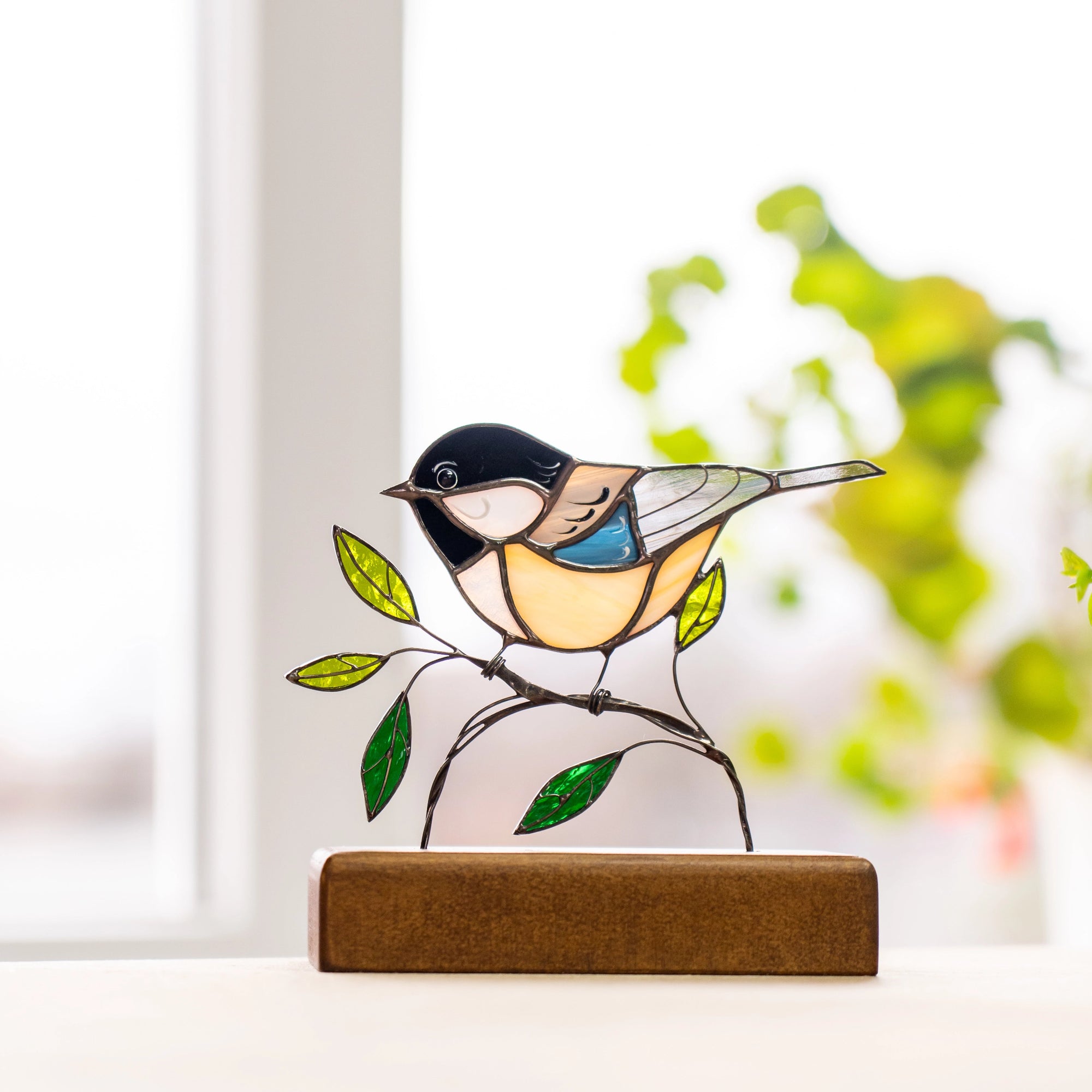 Stained glass chickadee bird glowing near window with green leaf accents