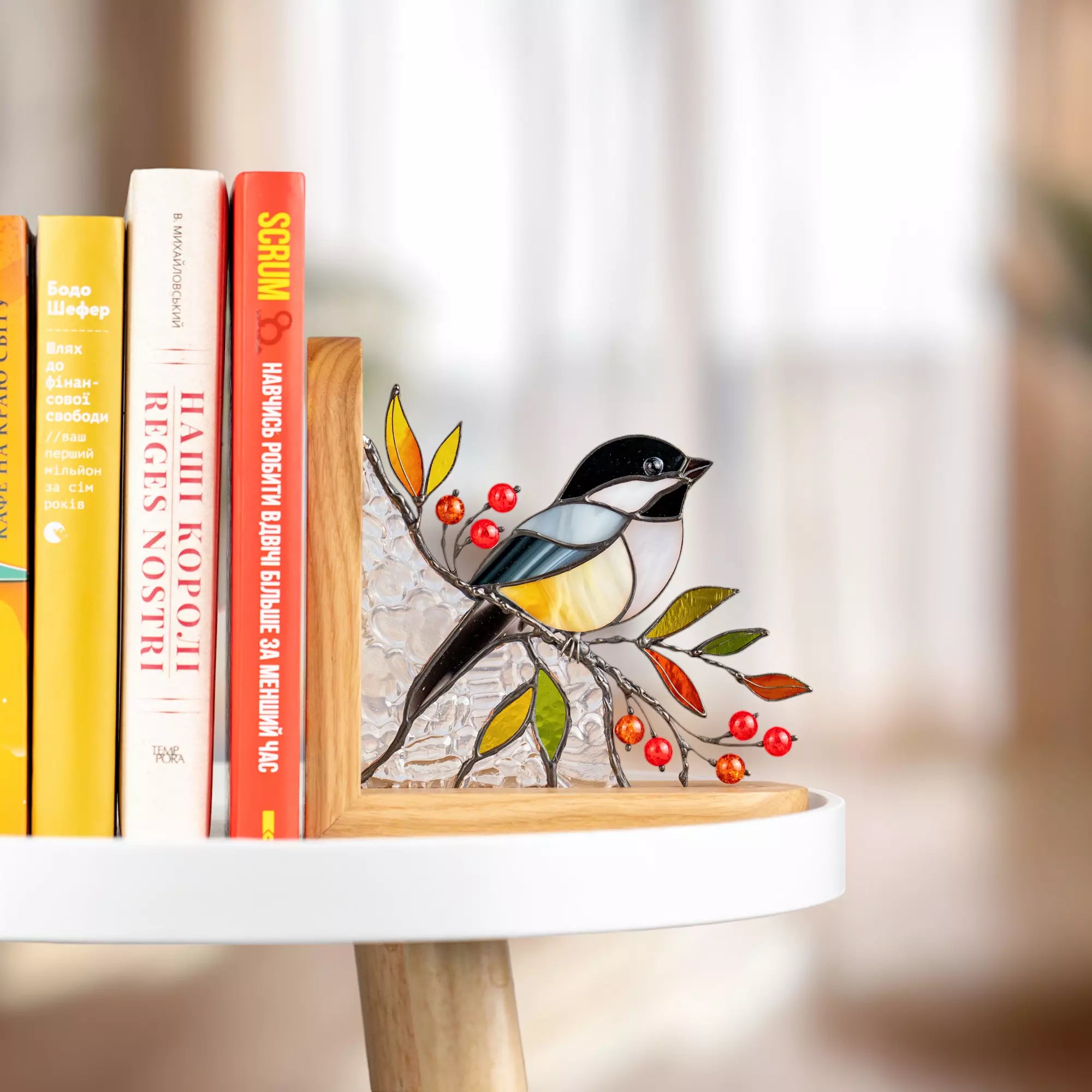 Stained glass chickadee bird art on a branch with red berries and green leaves, displayed indoors in soft daylight.