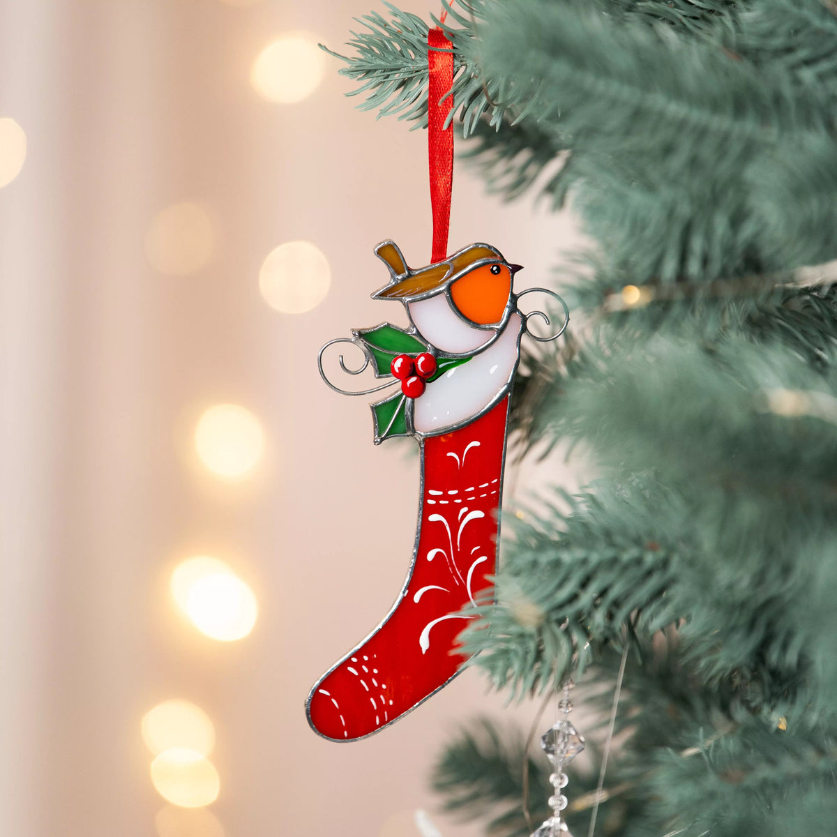 Stained glass Christmas ornament with an american robin bird on a red stocking hanging from a tree.
