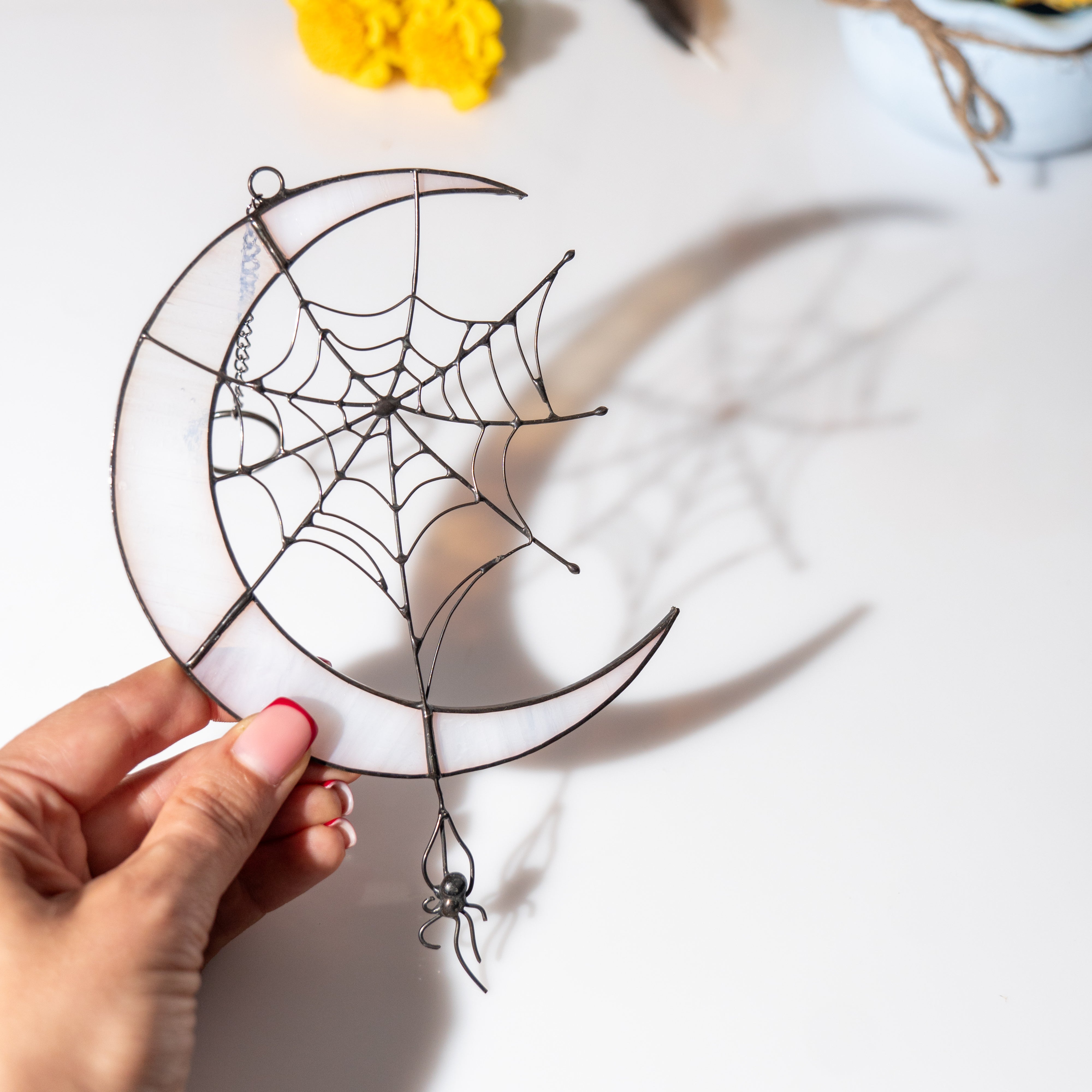 Handholding the stained glass spider web and moon suncatcher, shadow of the web cast on the surface below.