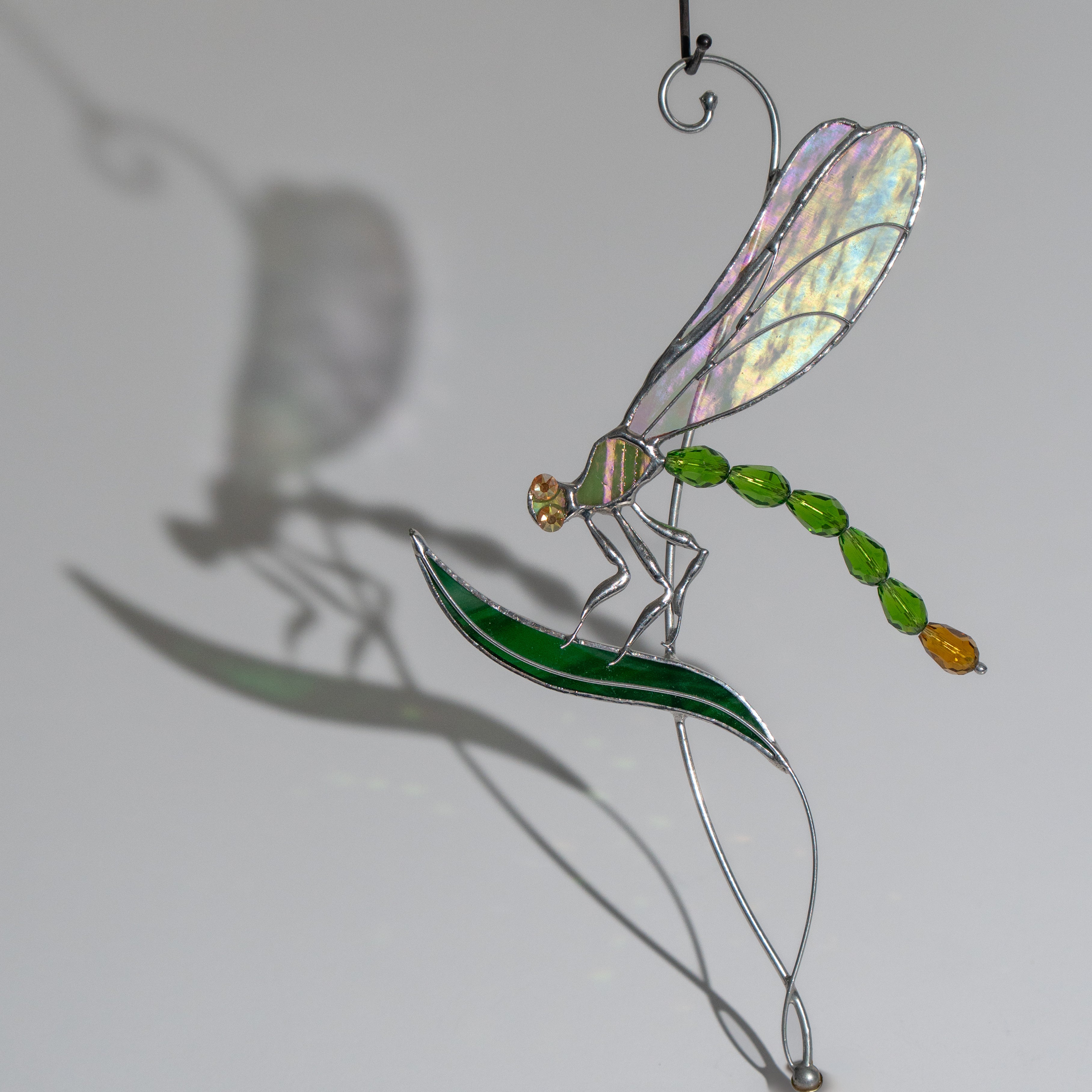 Detailed image of green dragonfly suncatcher on a leaf, light reflection and shadow visible on background wall.