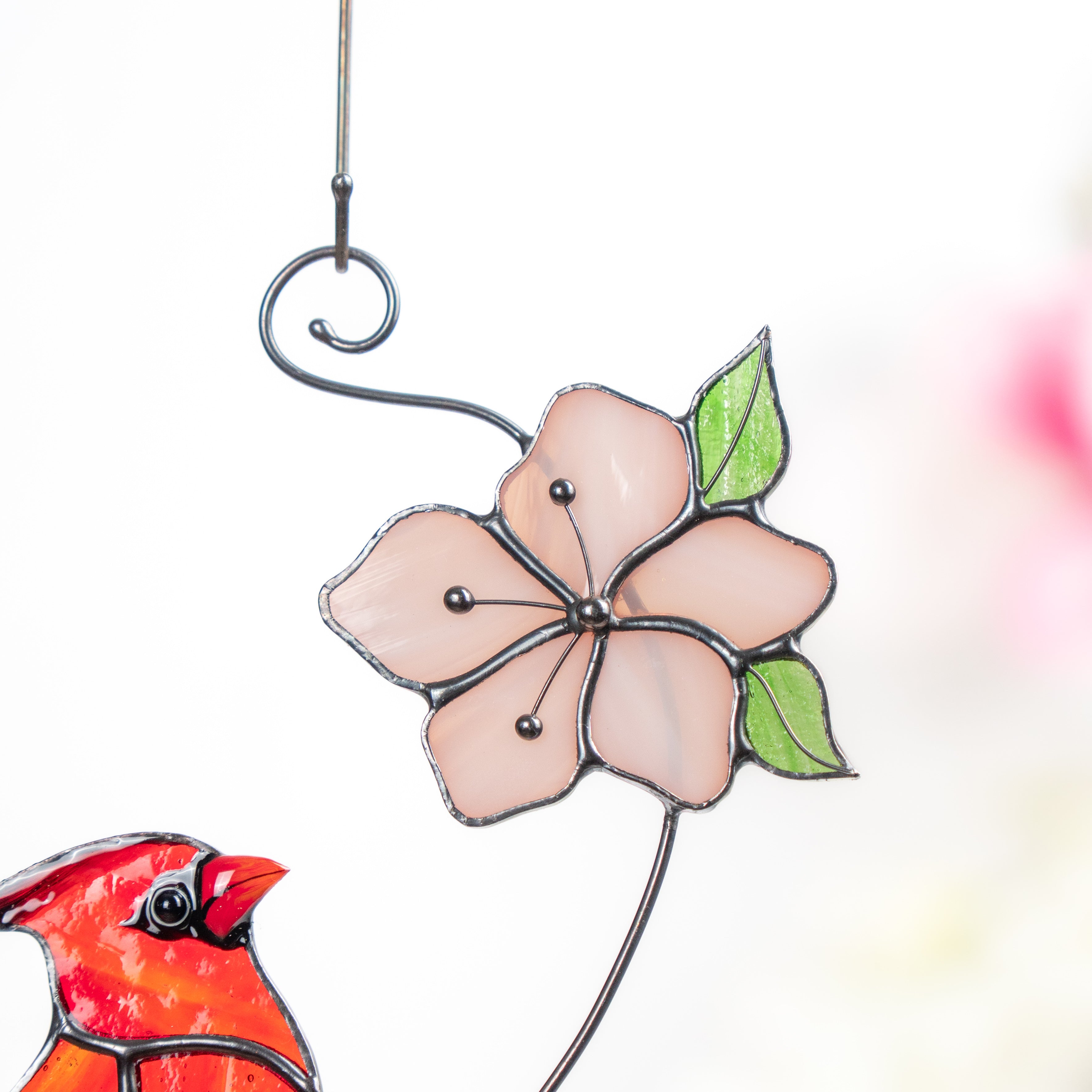 Detailed view of a delicate pink stained glass flower with fresh green leaves.
