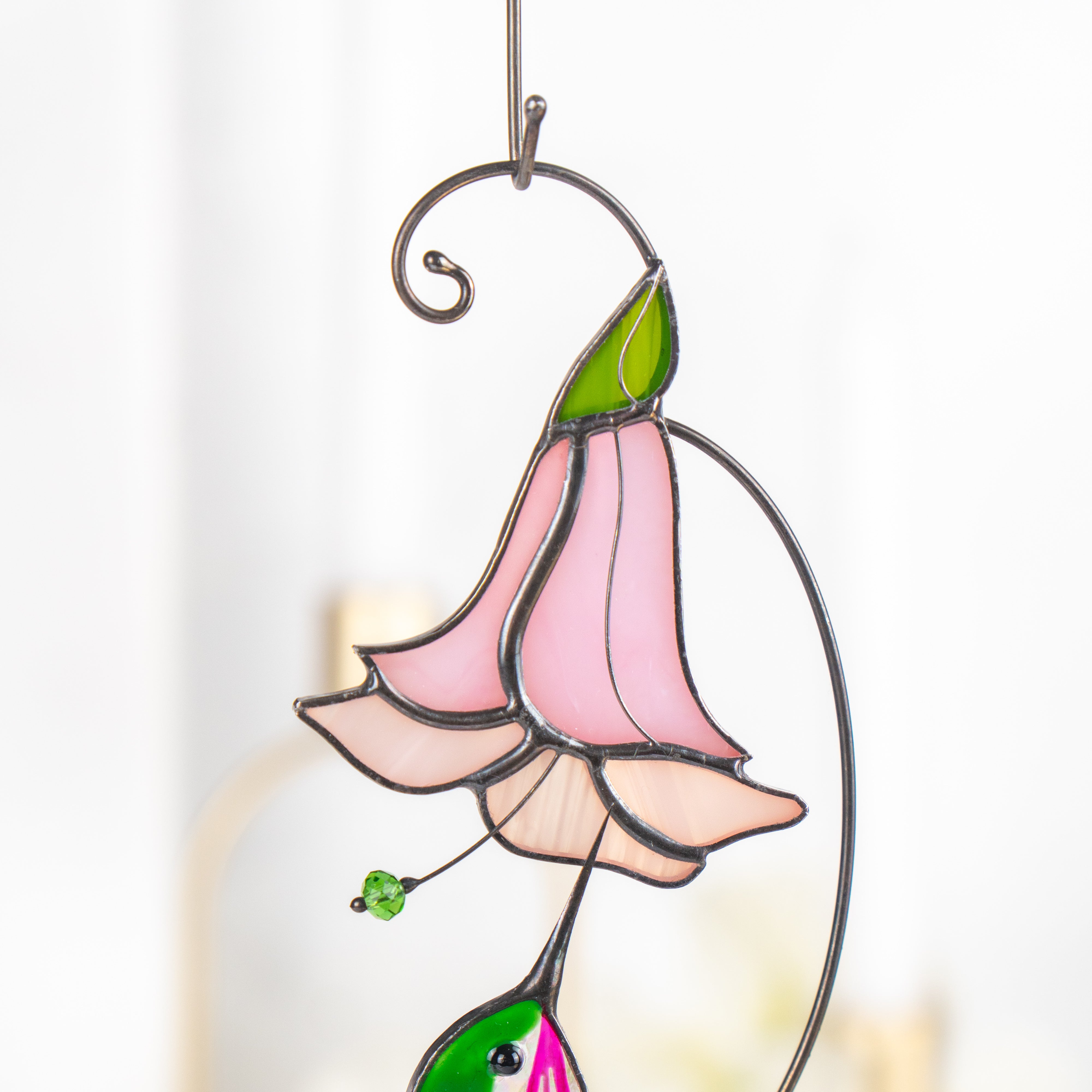 Detailed image of the pink stained glass flower with green leaf, part of the hummingbird and flower design.