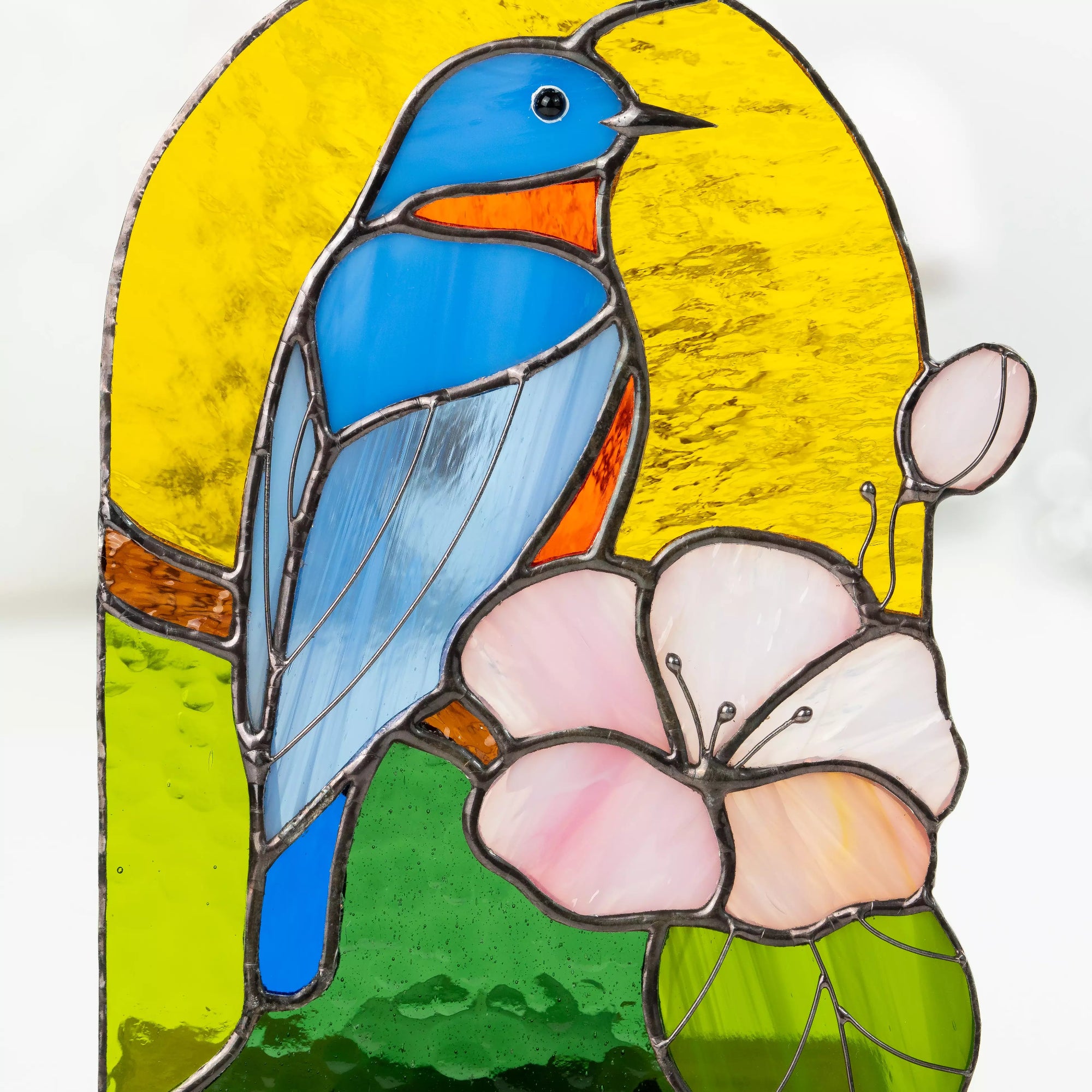Detail of stained glass featuring a bluebird and pale pink flower with green leaves