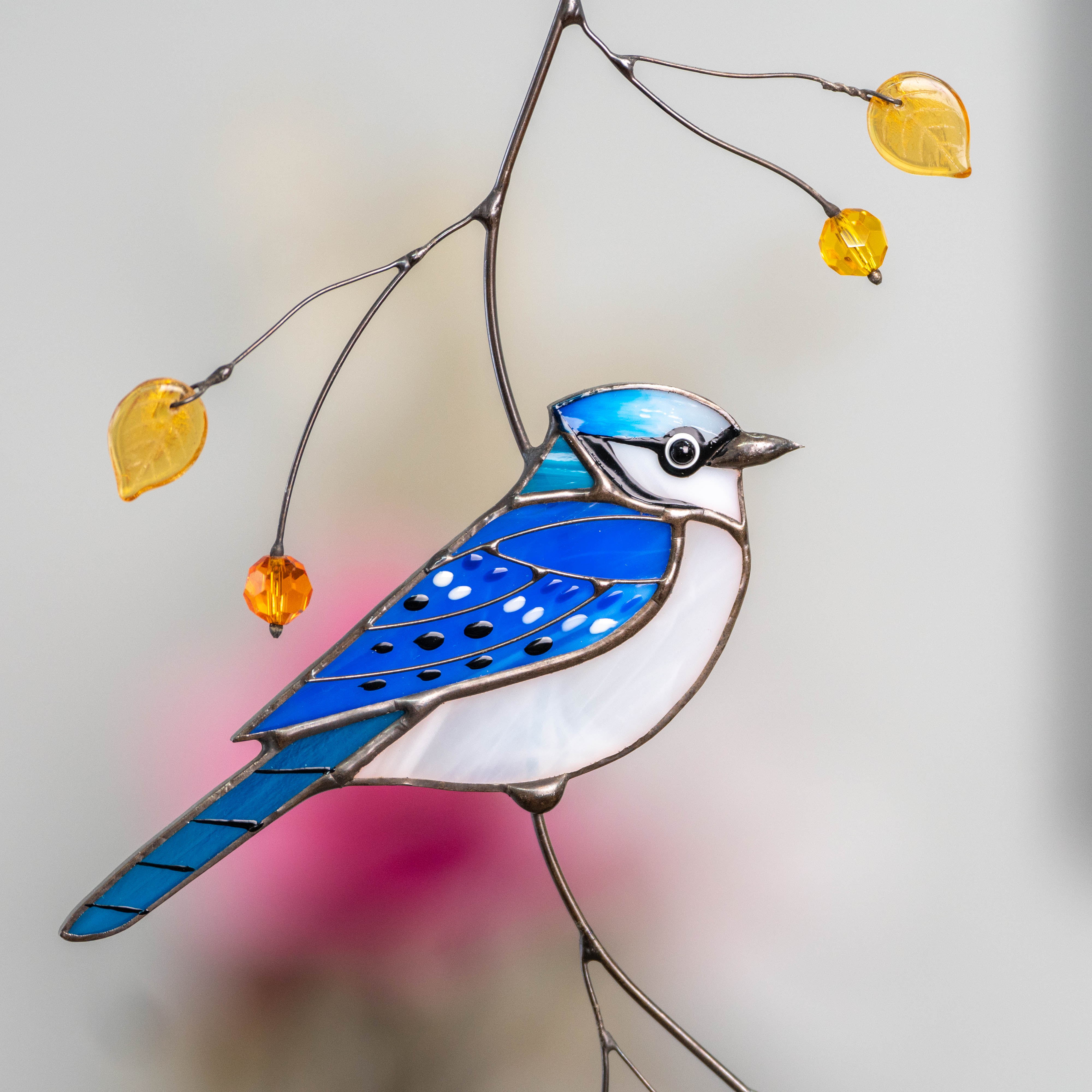 Detailed view of a stained glass blue jay’s head and beads with a bright green background.
