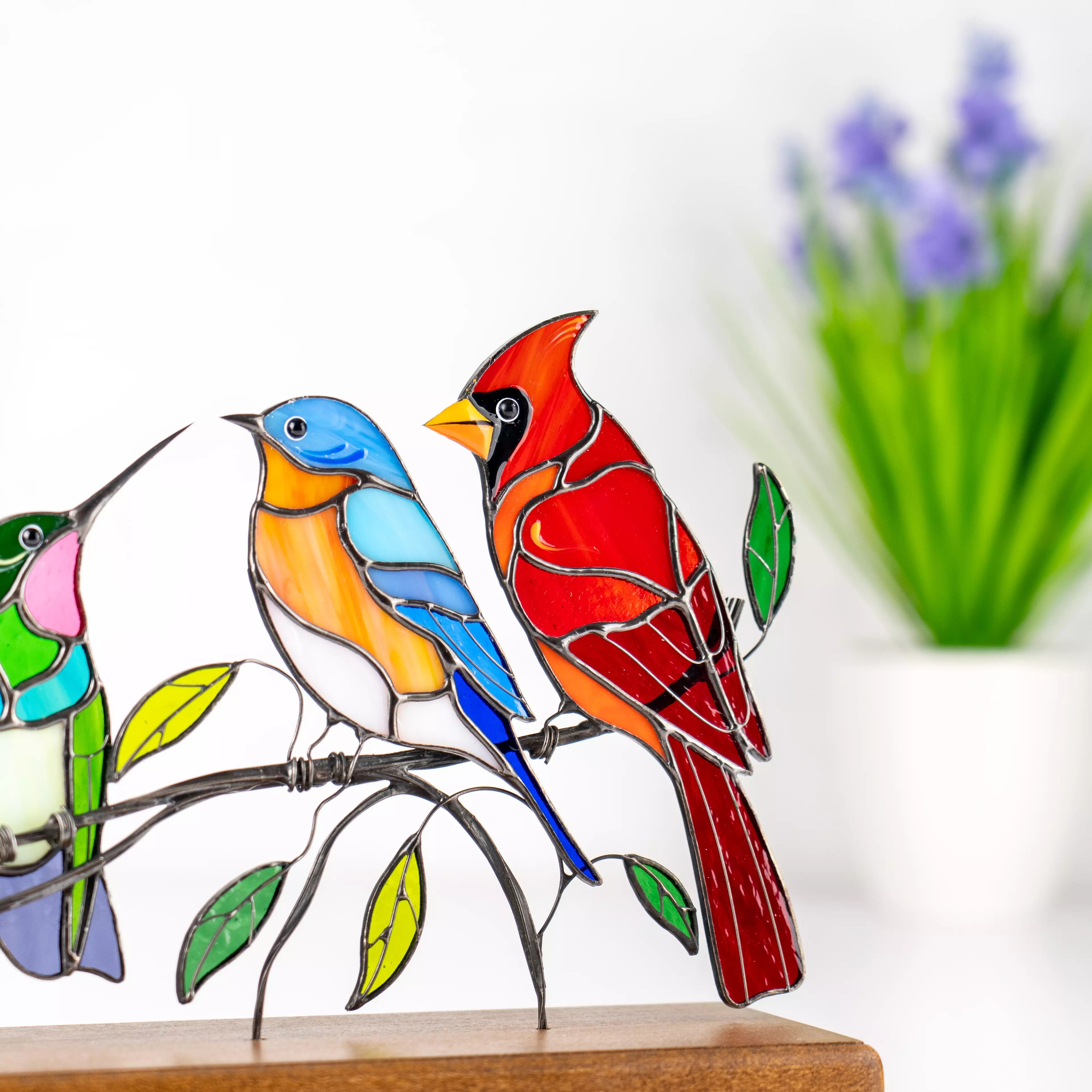 Detail of stained glass bluebird and cardinal sitting on branch with green leaves